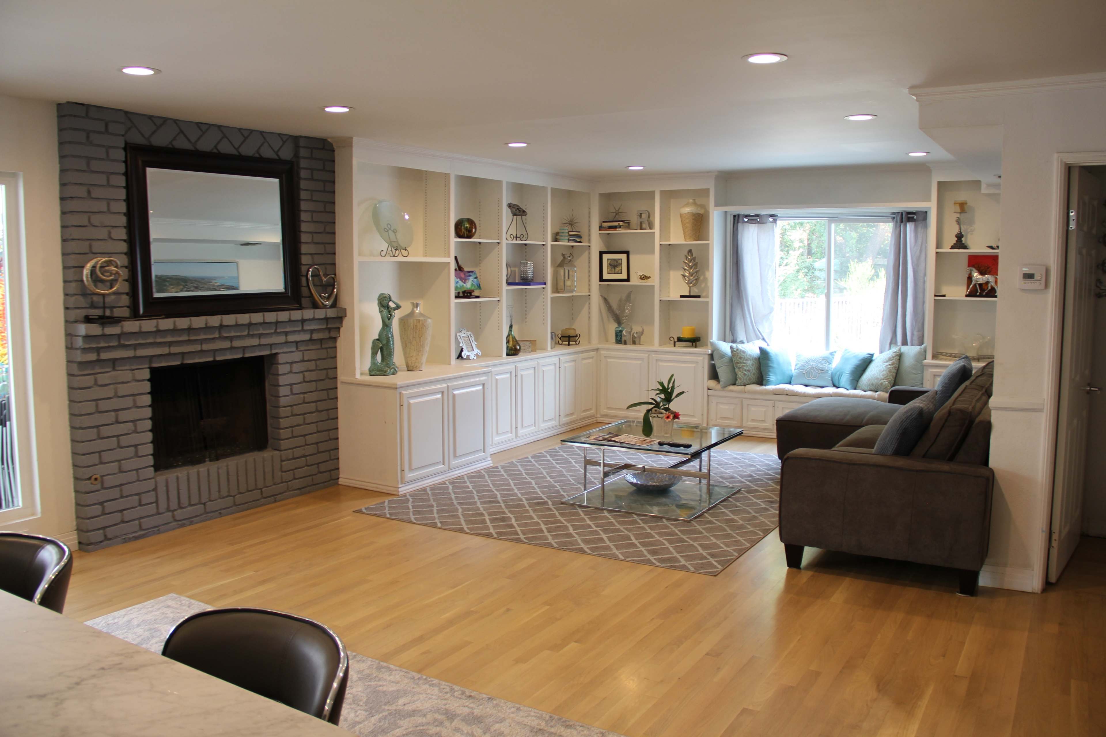 The image shows a spacious living room featuring a gray brick fireplace, built-in shelves with various decorative items, and a seating area with a sectional sofa and coffee table.
