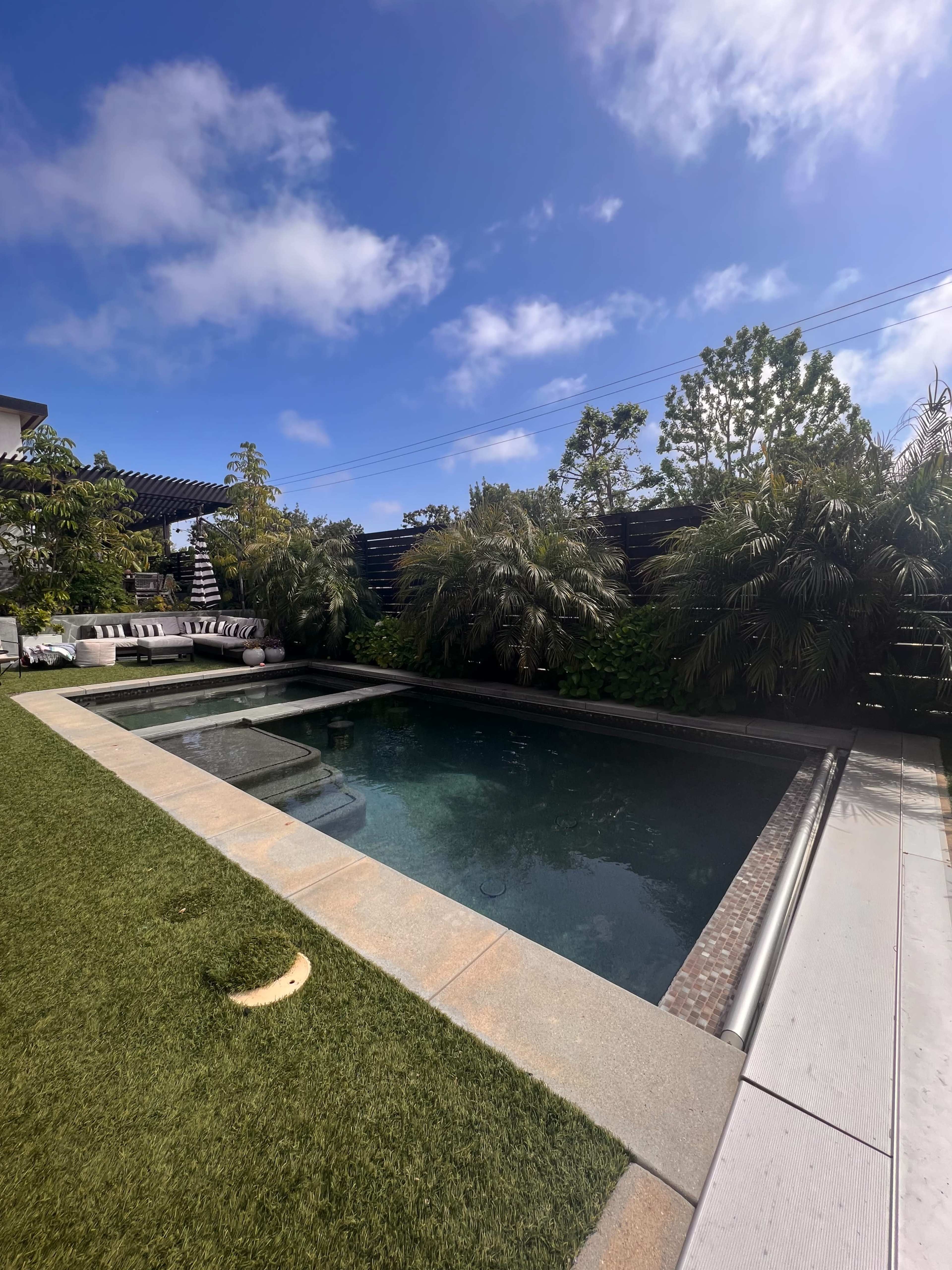 A modern backyard with a swimming pool surrounded by greenery and a neatly trimmed lawn.