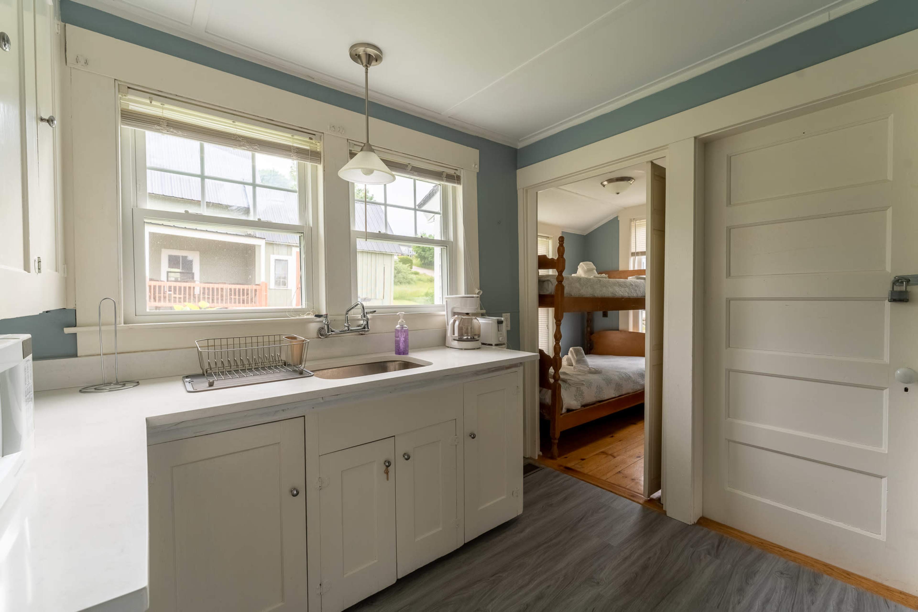 A kitchen with white cabinets, a sink, and a doorway leading to a room with bunk beds.