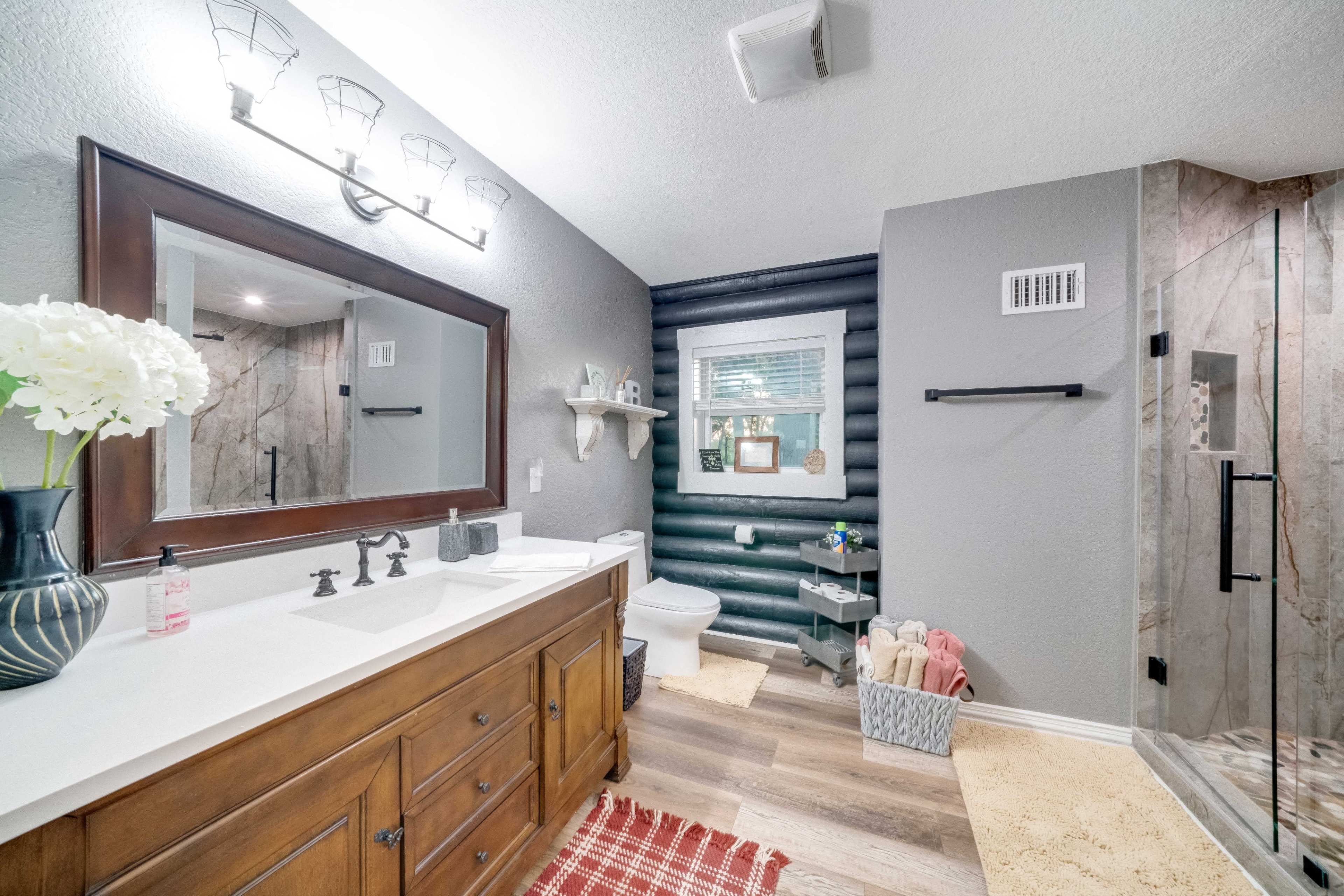 The image shows a modern bathroom with a double sink vanity, a glass shower enclosure, and a mixture of dark and light-colored walls.