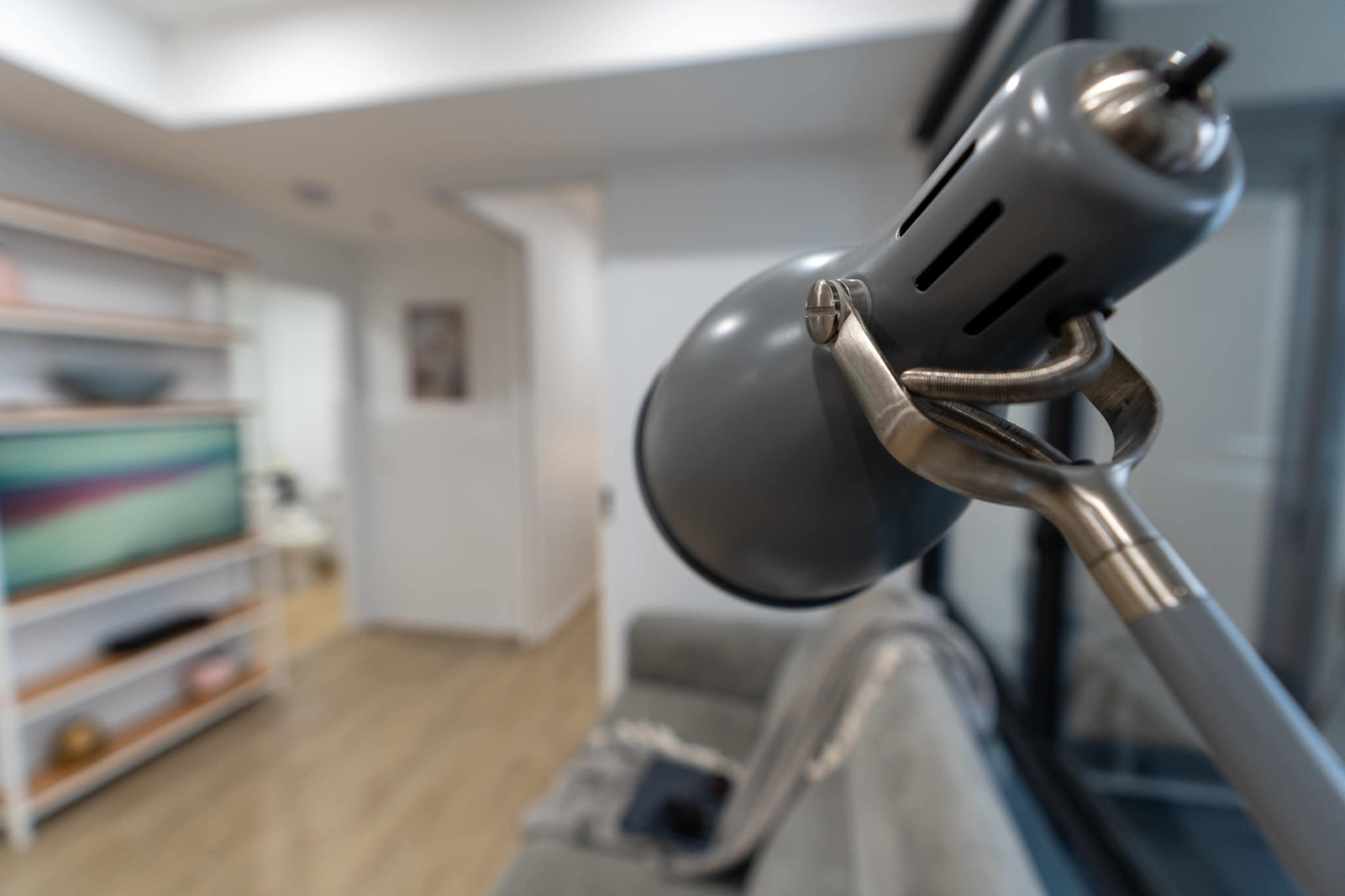 A gray desk lamp is positioned prominently in the foreground, with a living space featuring a couch and a television visible in the background.