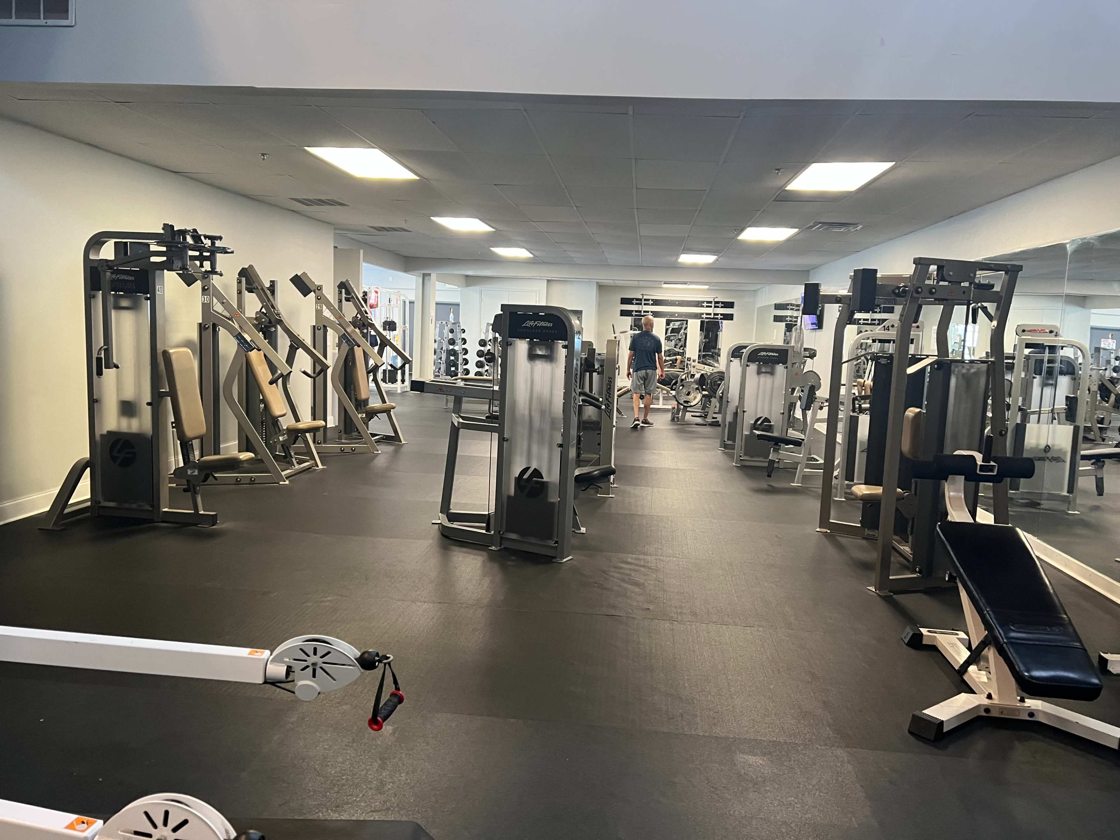 A spacious gym interior with various exercise equipment and a person walking towards the back.