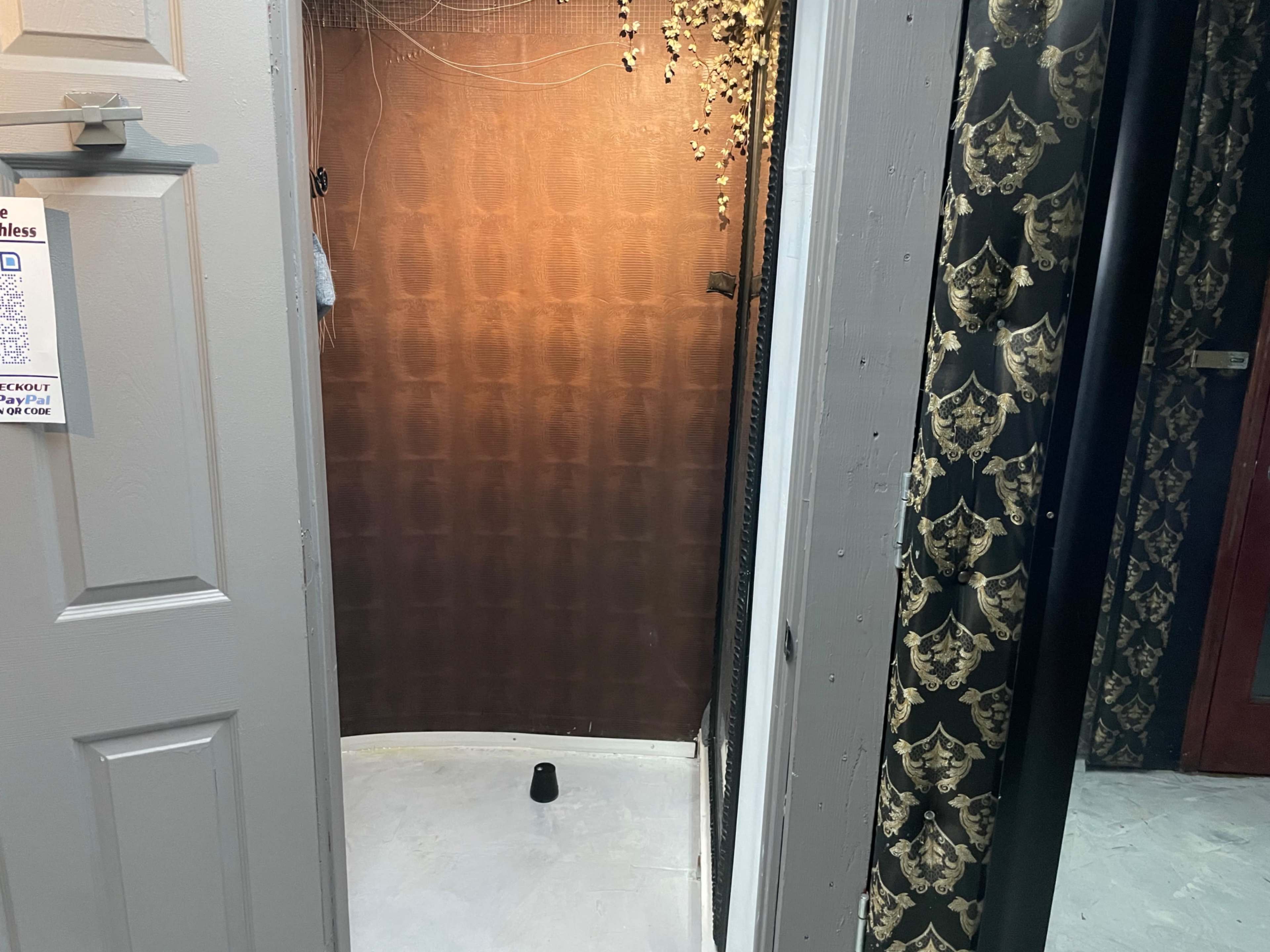 The image shows a small, empty room with a dark patterned wall, a light-colored floor, and an open door.