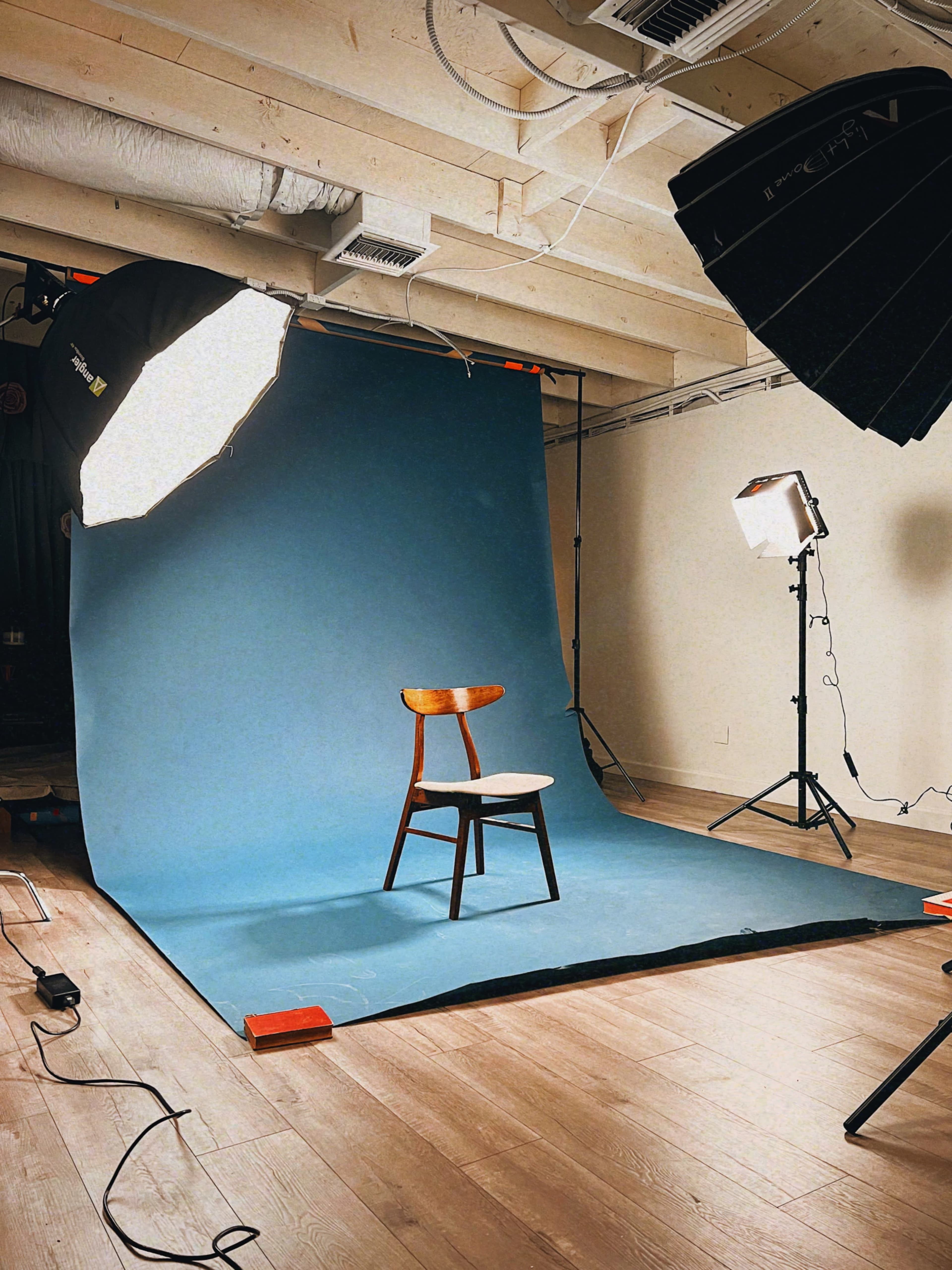 A wooden chair is positioned on a blue backdrop in a well-lit photography studio.