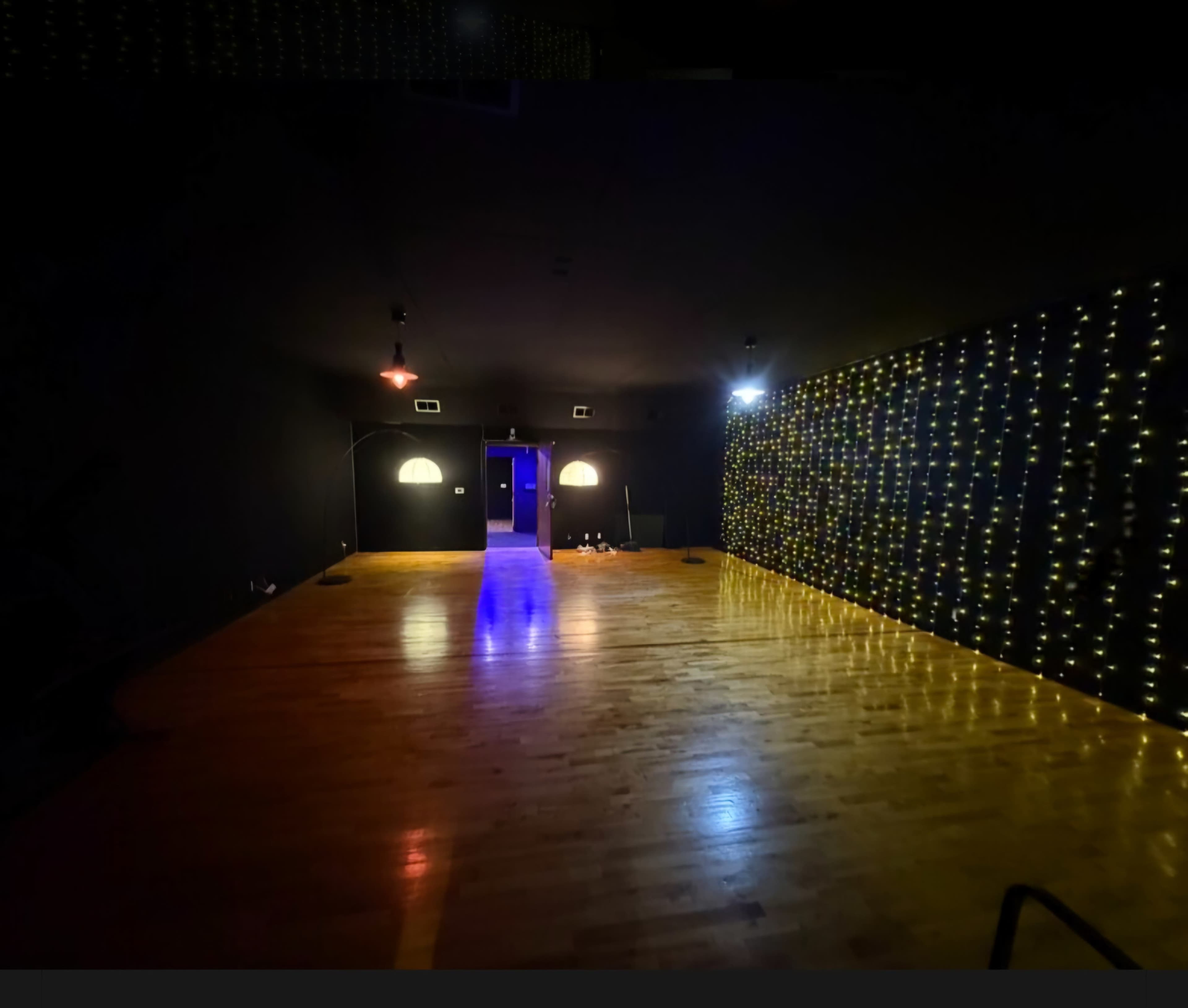 The image shows a dimly lit room with wooden flooring and a wall decorated with string lights, creating an inviting atmosphere.
