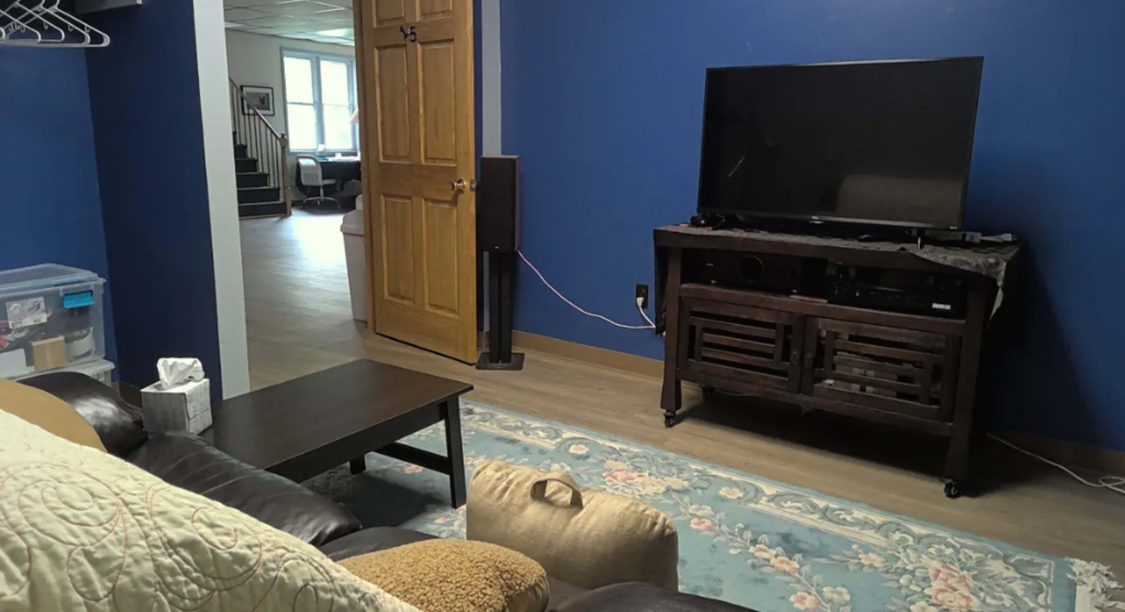 A living room with a brown couch, a wooden coffee table, a television on a cabinet, and a doorway leading to another room.