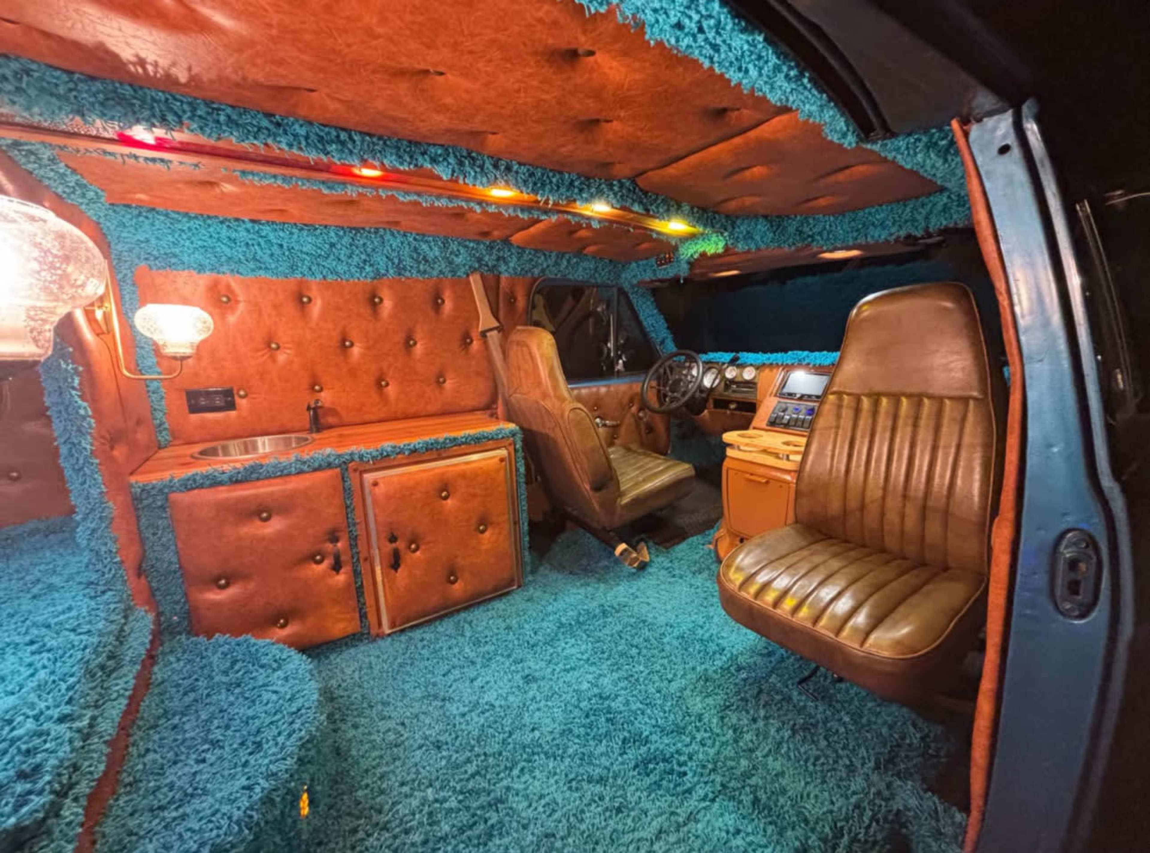The interior of a van is adorned with bright blue shag carpeting and brown leather upholstery.