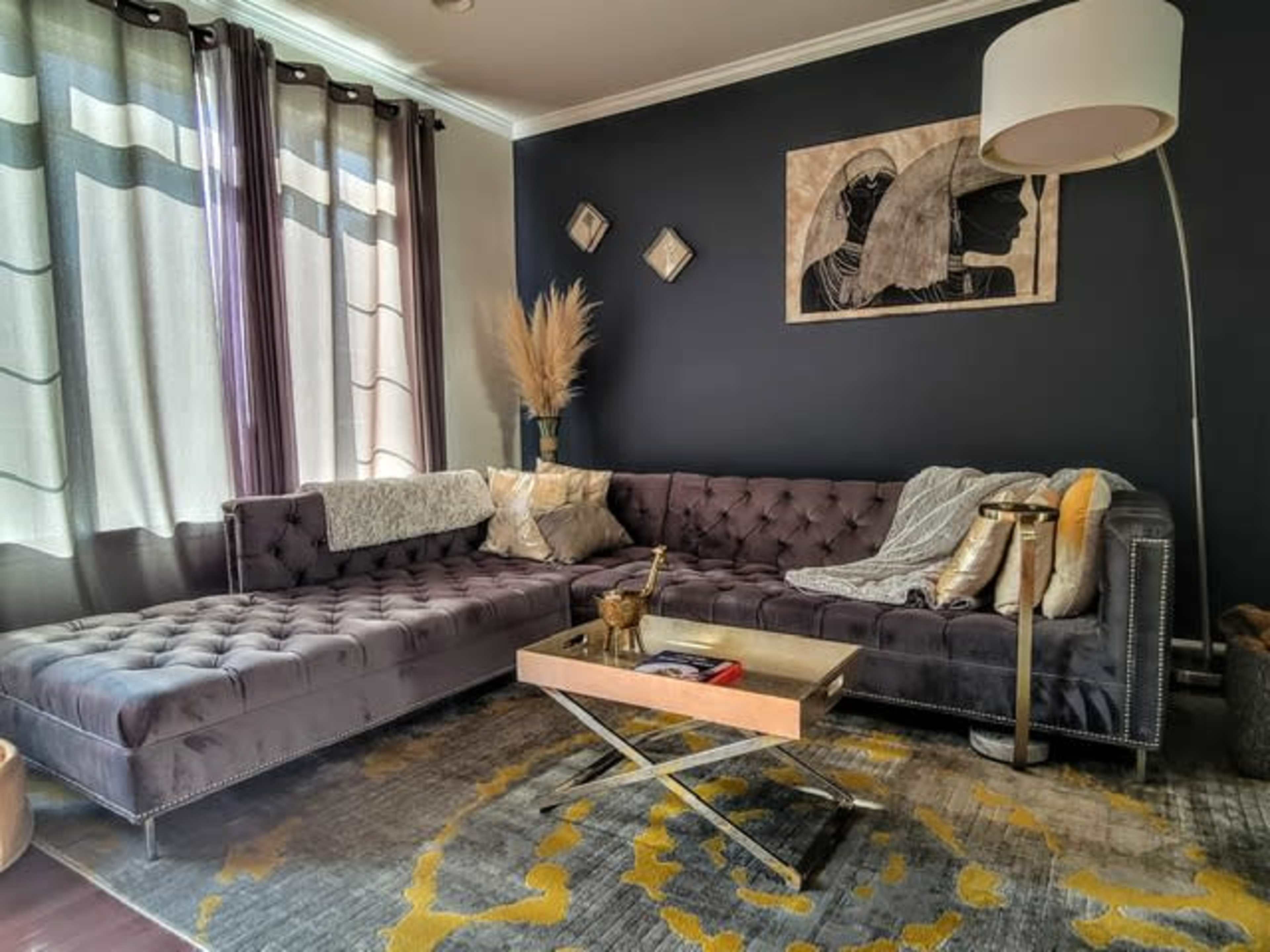 A modern living room features a dark wall, a plush sectional sofa with cushions, a coffee table, and decorative elements like plants and artwork.