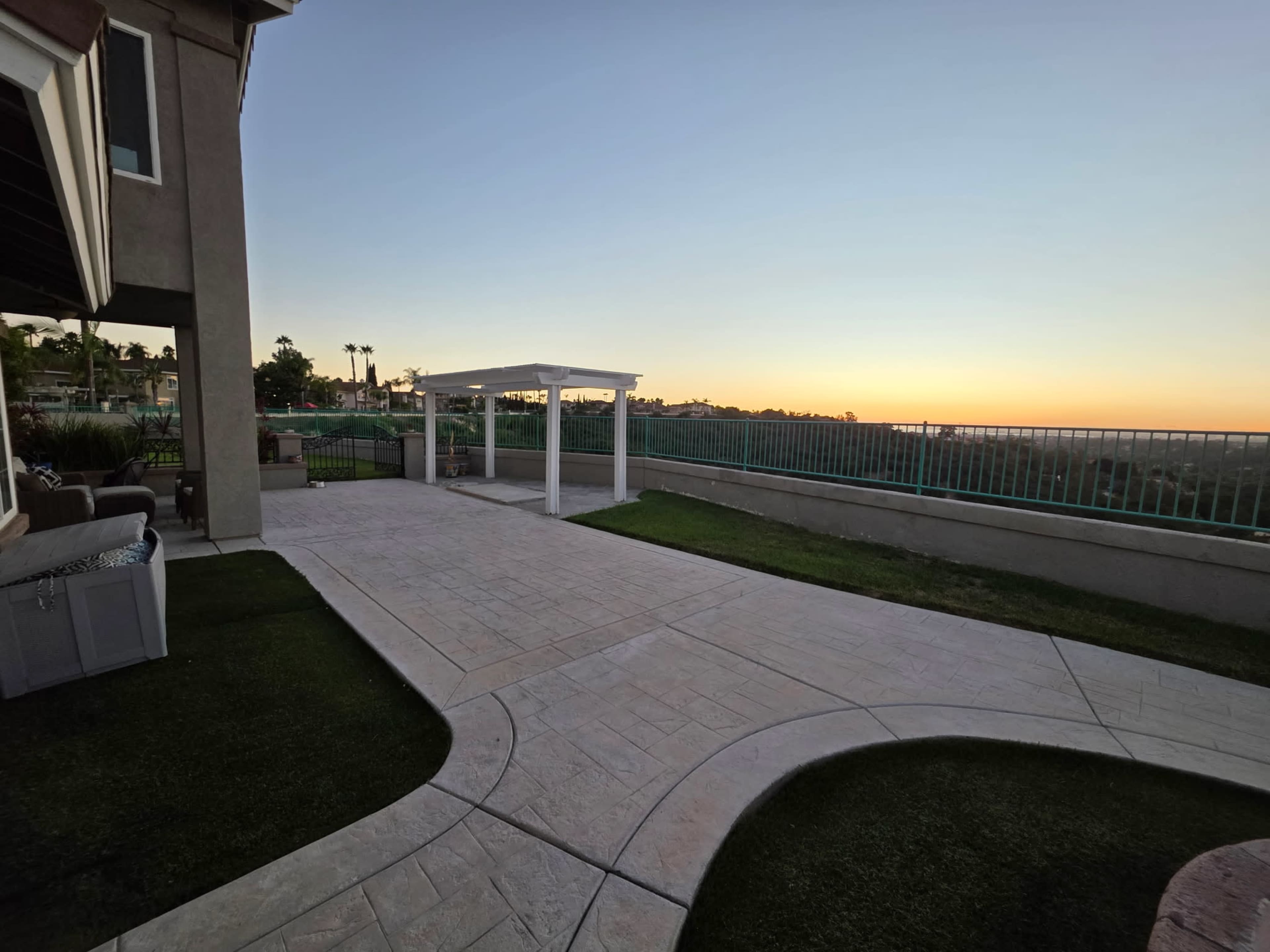 The image shows a backyard patio with a white gazebo and a view of a sunset over a landscaped lawn and fence.