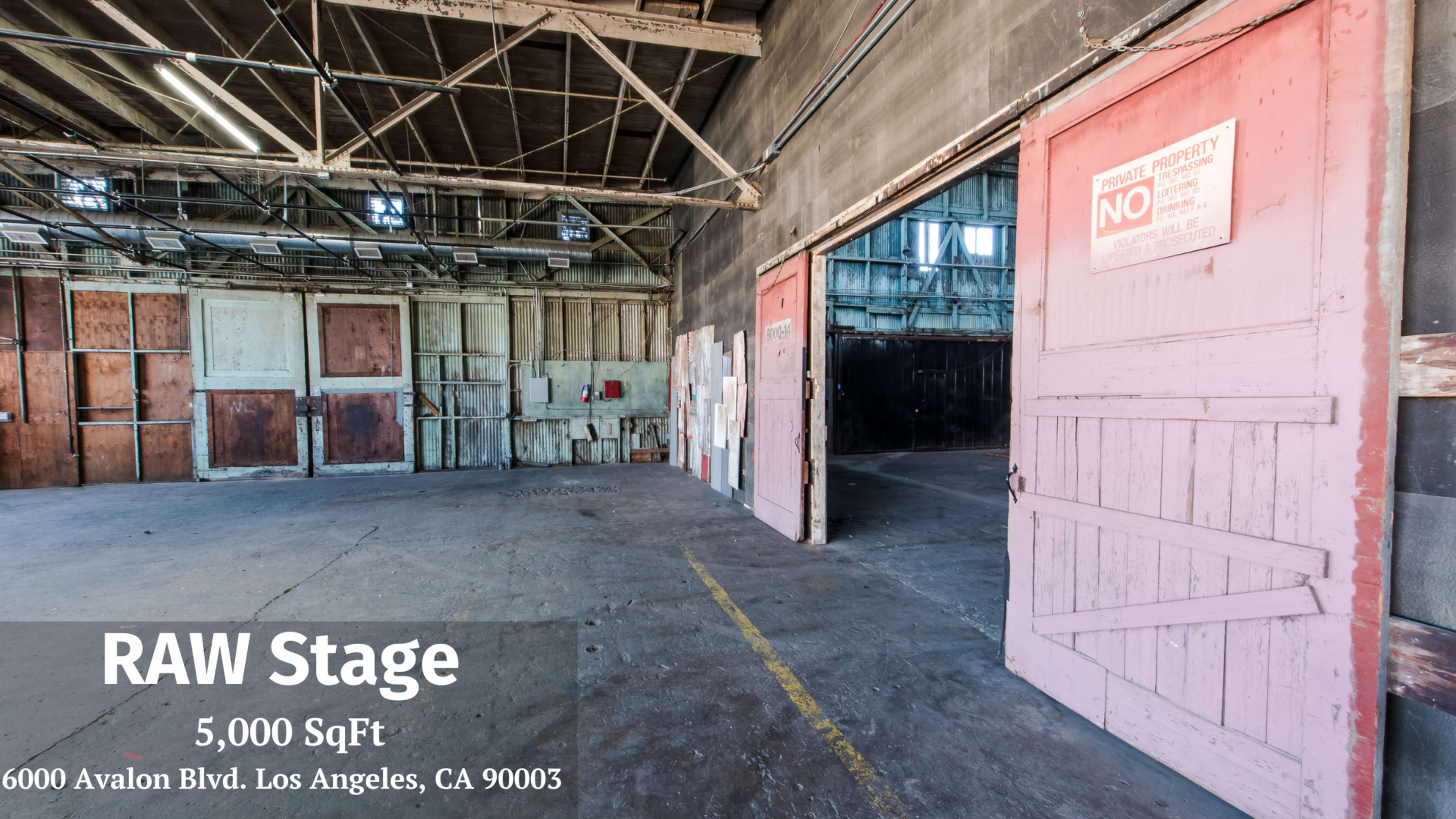 The image shows a spacious, empty warehouse with large double doors and a concrete floor, featuring peeling paint and industrial elements.