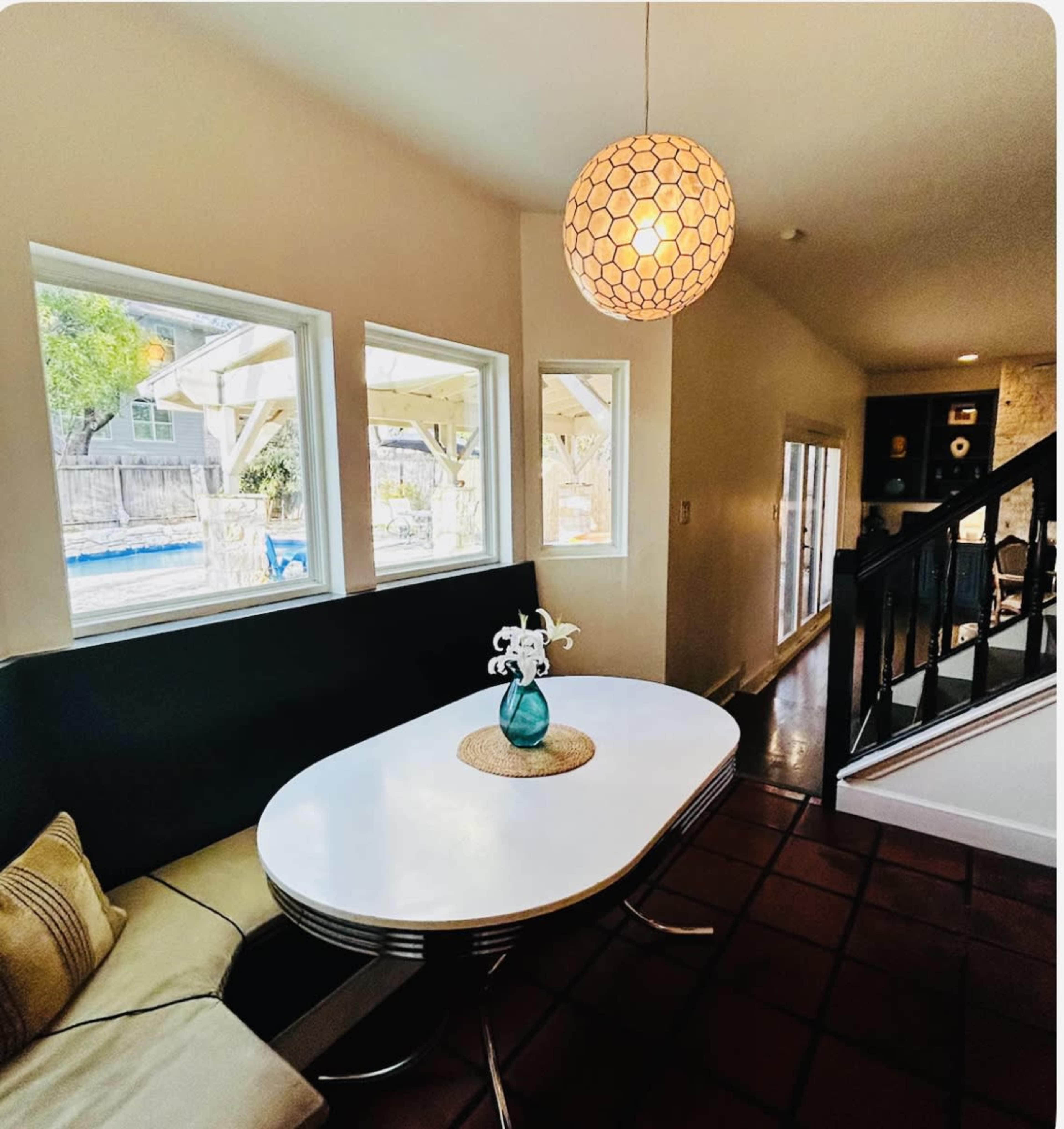 A modern dining area features a white oval table with a glass vase on it, surrounded by a built-in bench and well-lit by a pendant light.