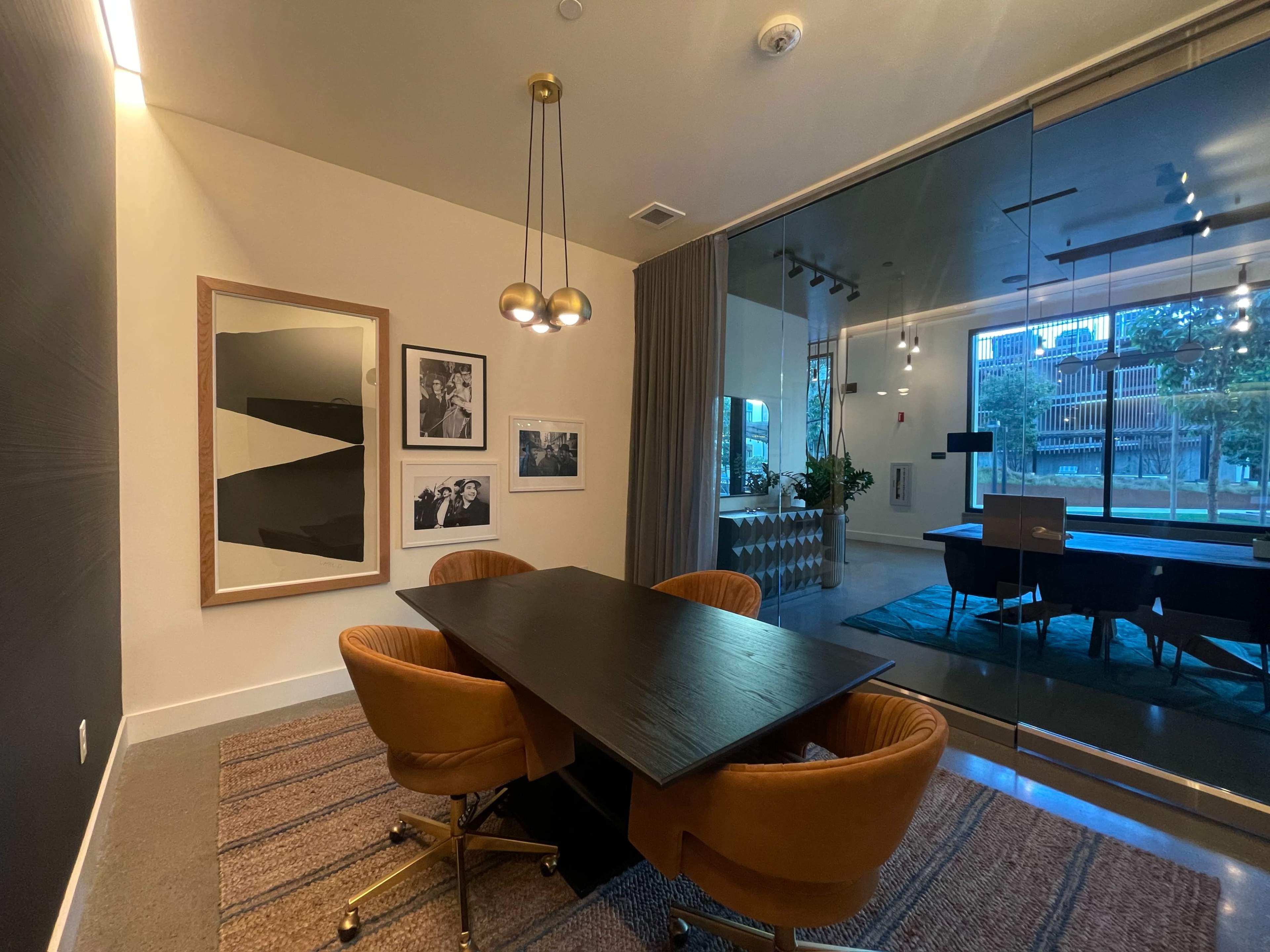 A modern conference room featuring a dark table surrounded by four brown chairs and large glass windows overlooking an outdoor area.