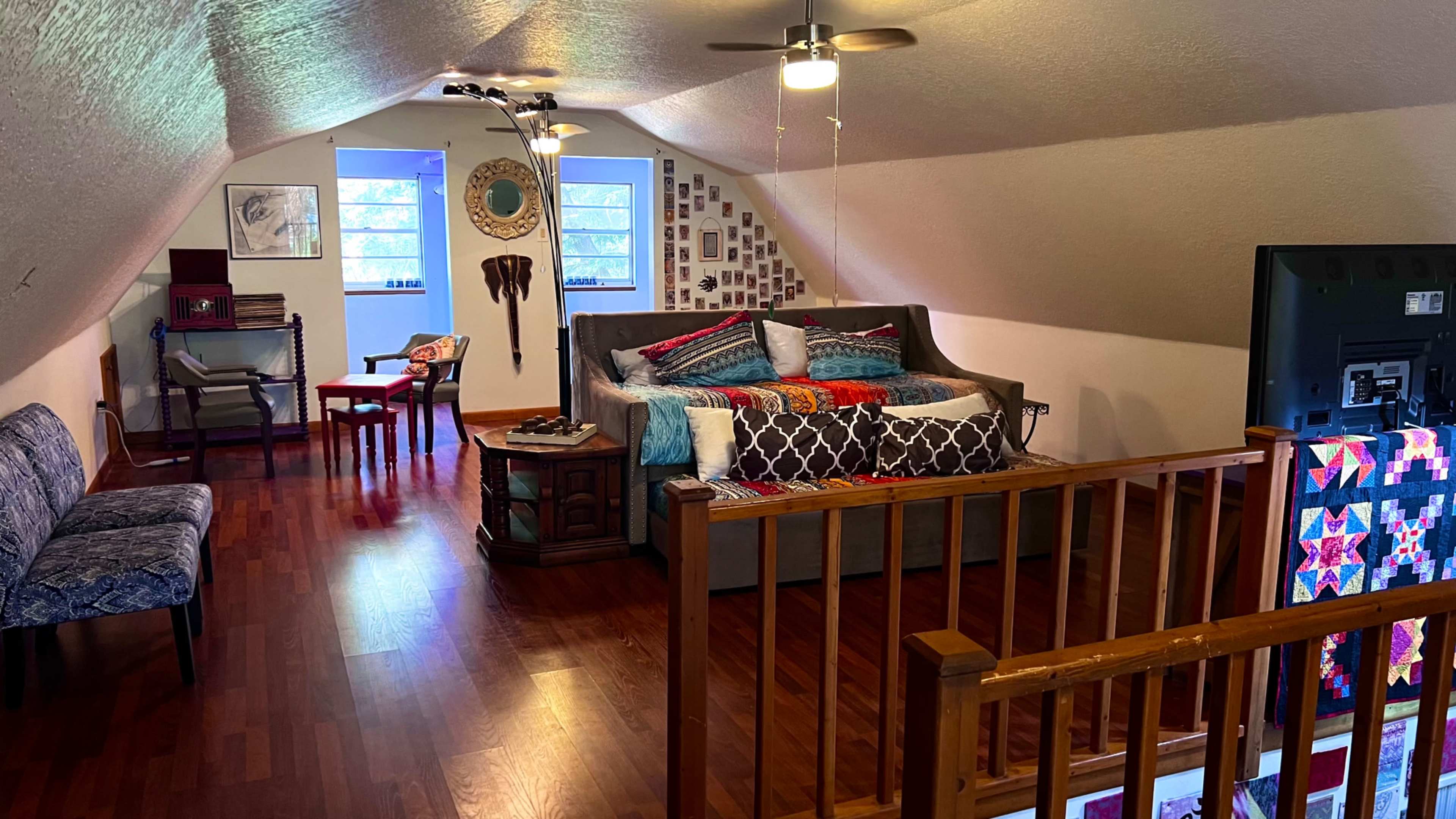 The image shows a cozy, furnished loft space with a bed, a seating area, and various decorative elements on the walls.