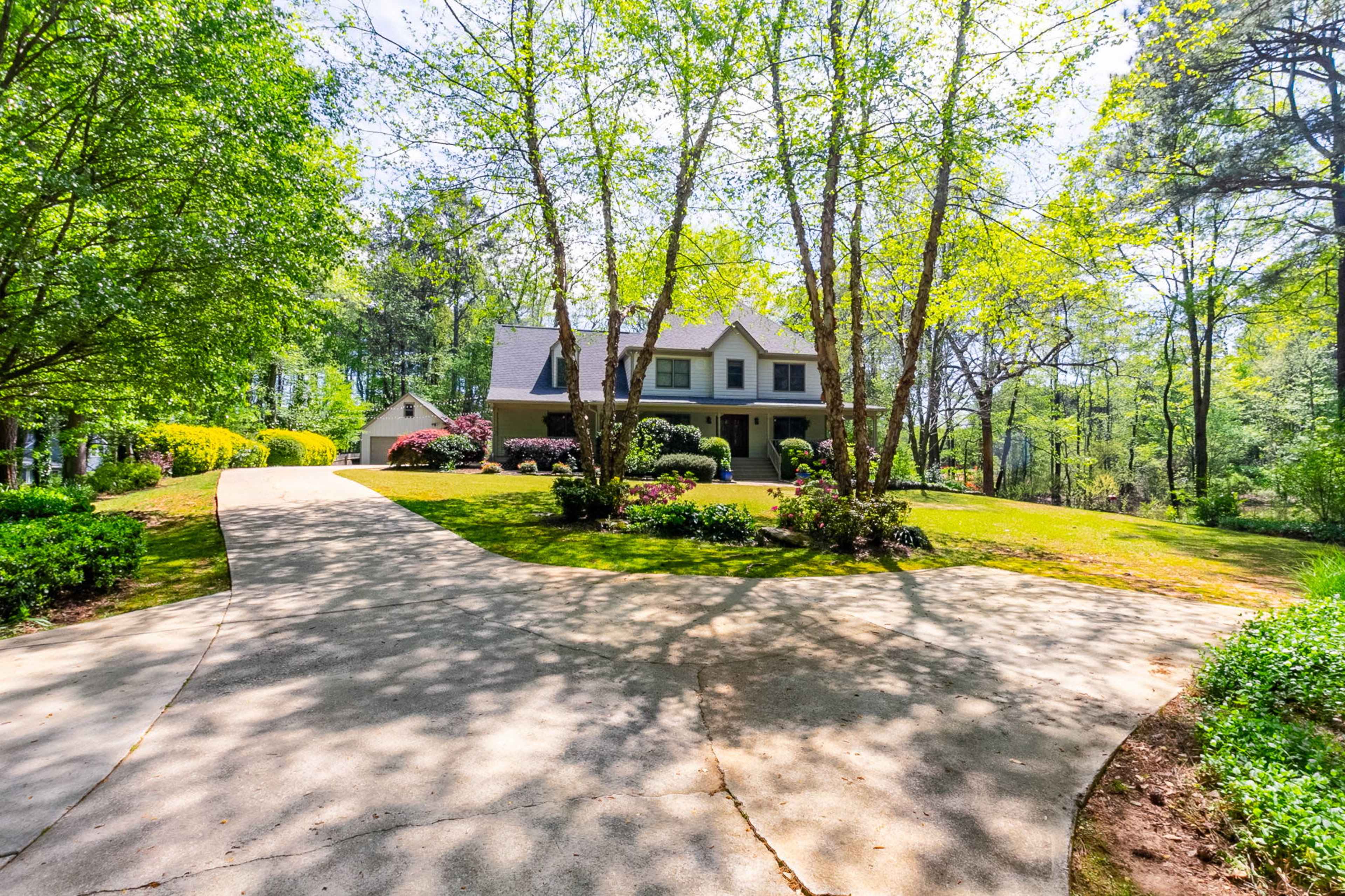 A house with a sloping driveway is surrounded by trees and landscaped gardens.