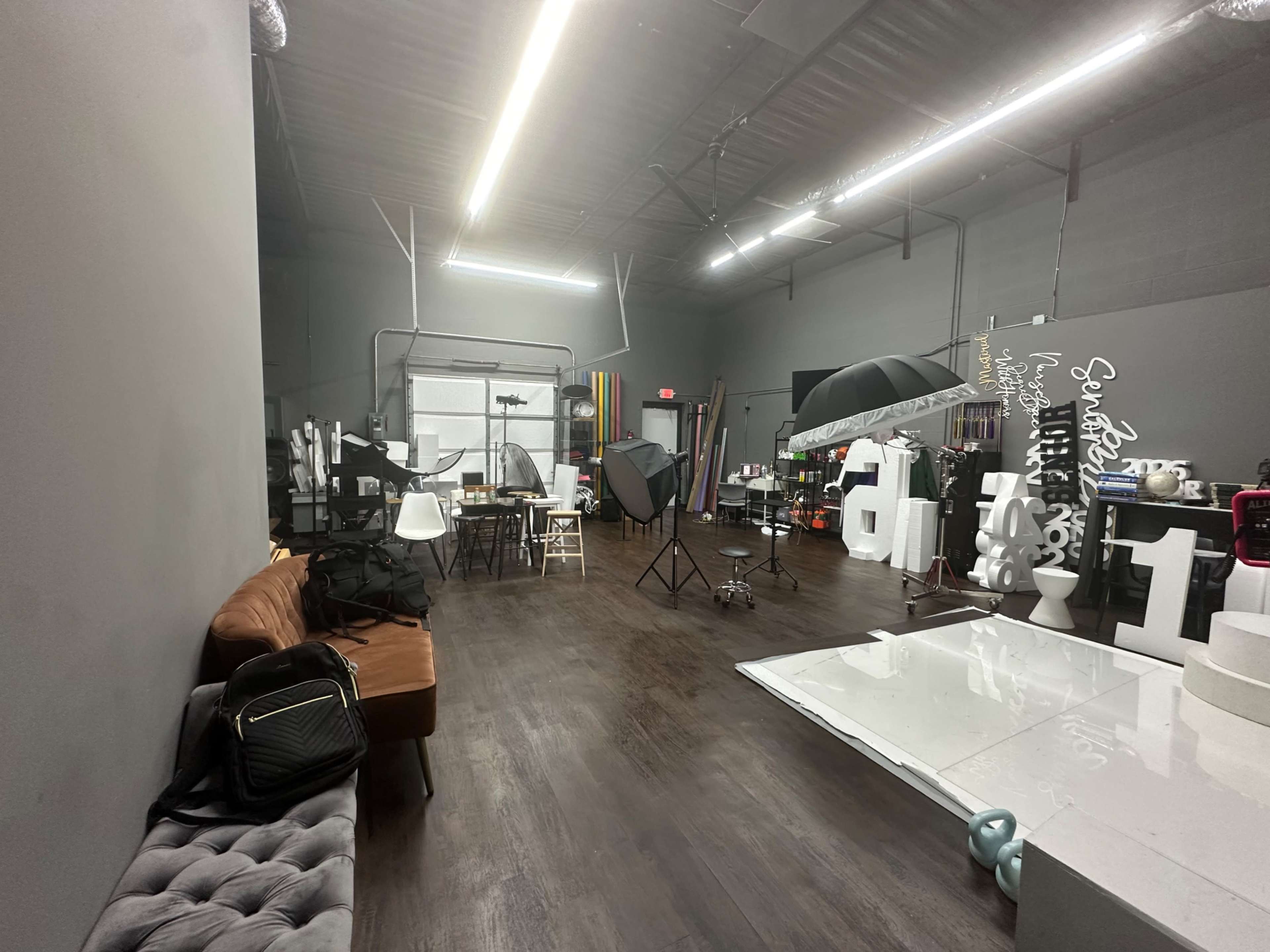 The image shows a spacious studio with various photography equipment, a seating area, and different props set up for a photoshoot.