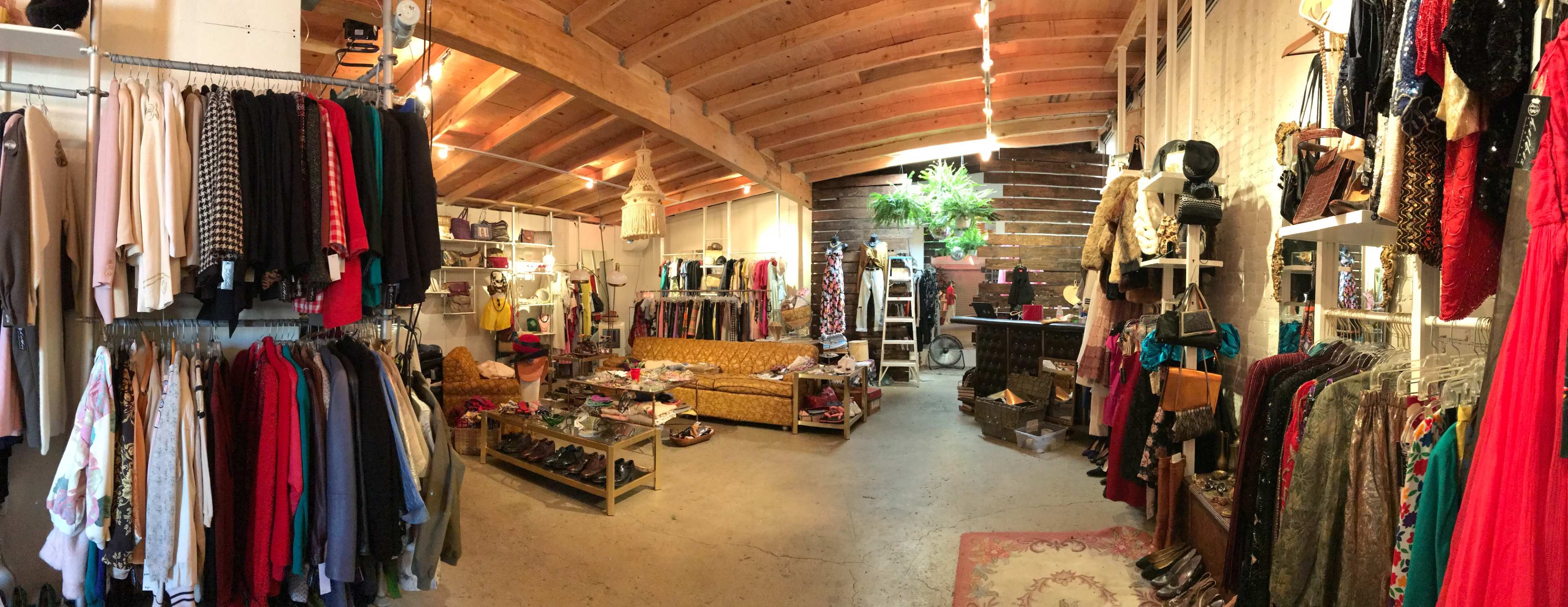 The image shows a boutique interior with clothing racks, a seating area, and various accessories displayed on shelves.