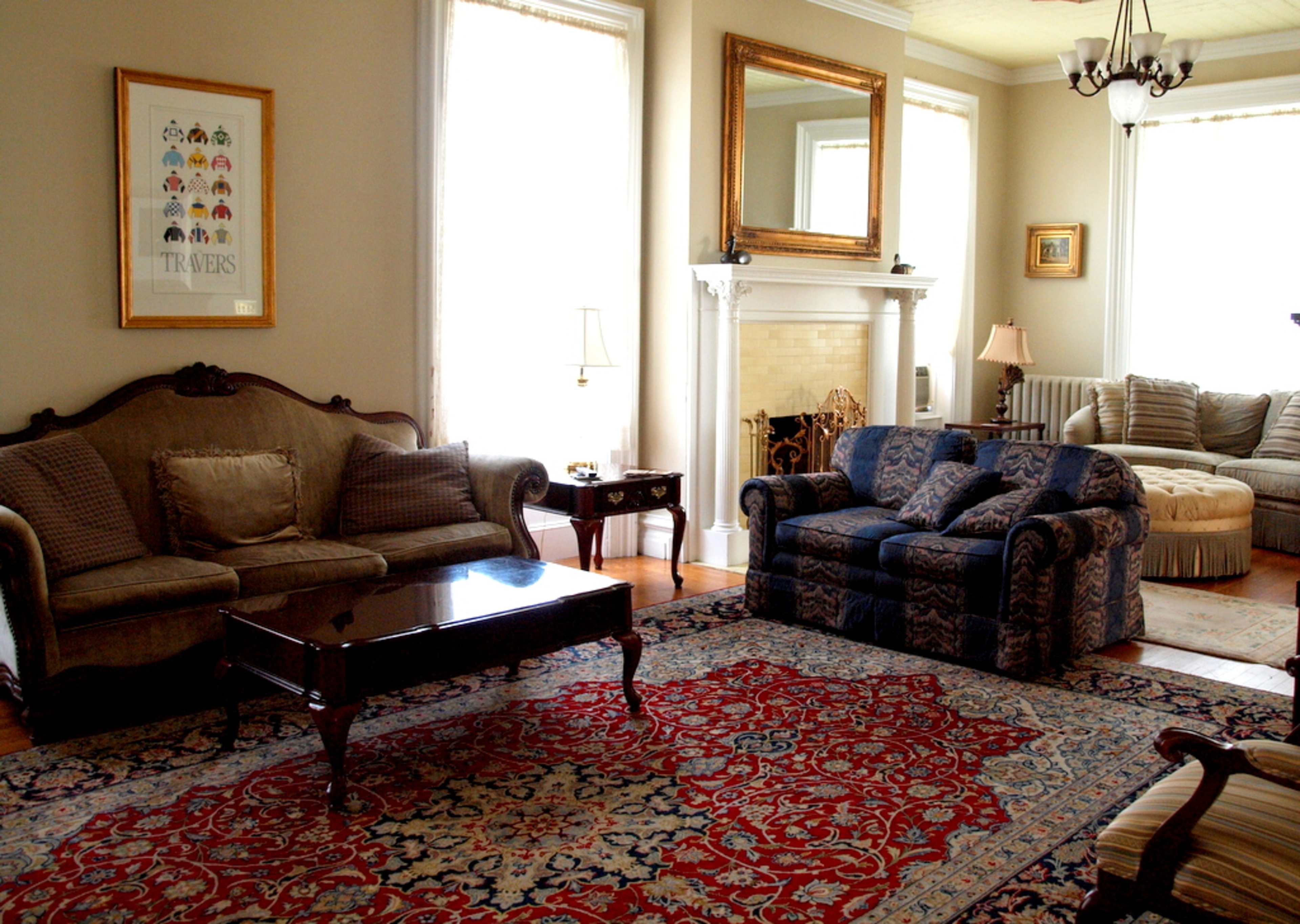 A living room with a patterned area rug, two sofas, a coffee table, and a fireplace surrounded by windows.