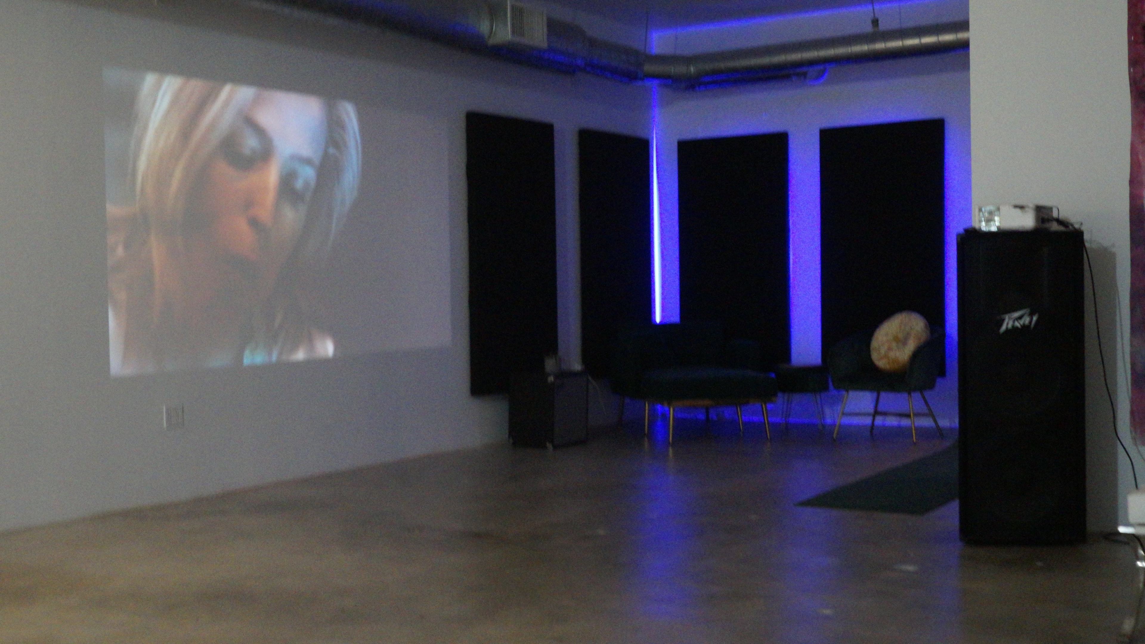 A modern room with a projected video on the wall, dark acoustic panels, a green couch, and a speaker in the corner.