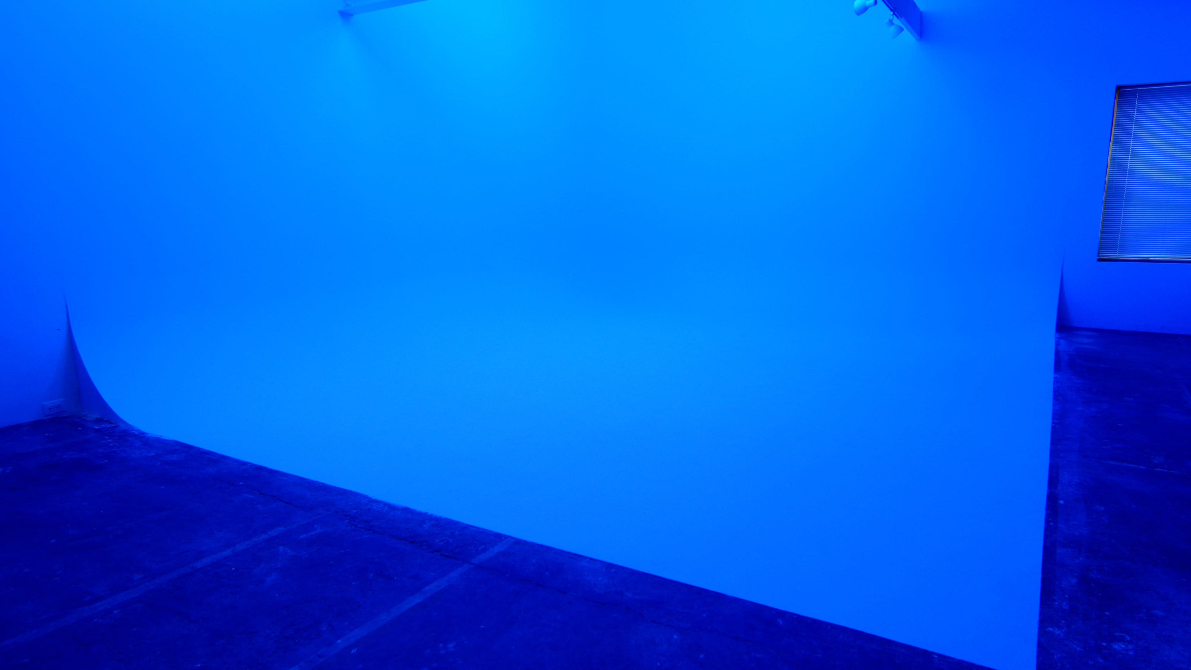 A minimalistic blue-lit studio space with a seamless backdrop and a concrete floor.