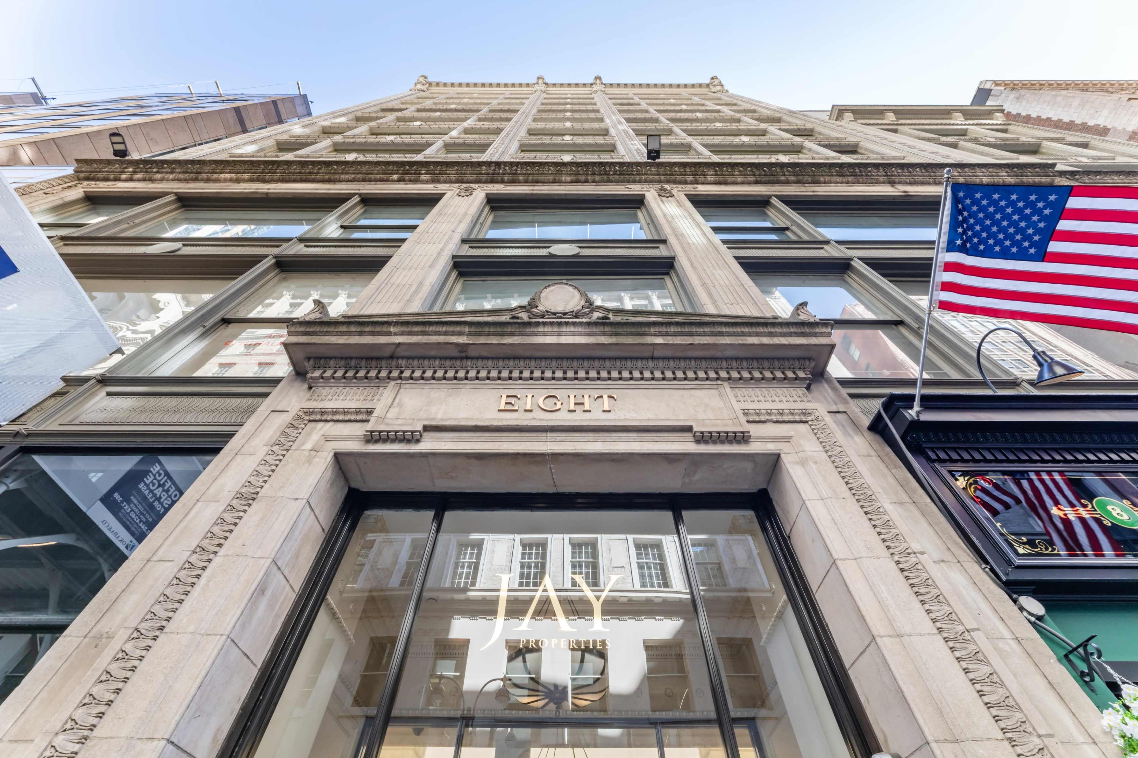 The image shows the exterior of a tall building with a decorative facade, featuring the word "EIGHT" above a large window and American flags on either side.