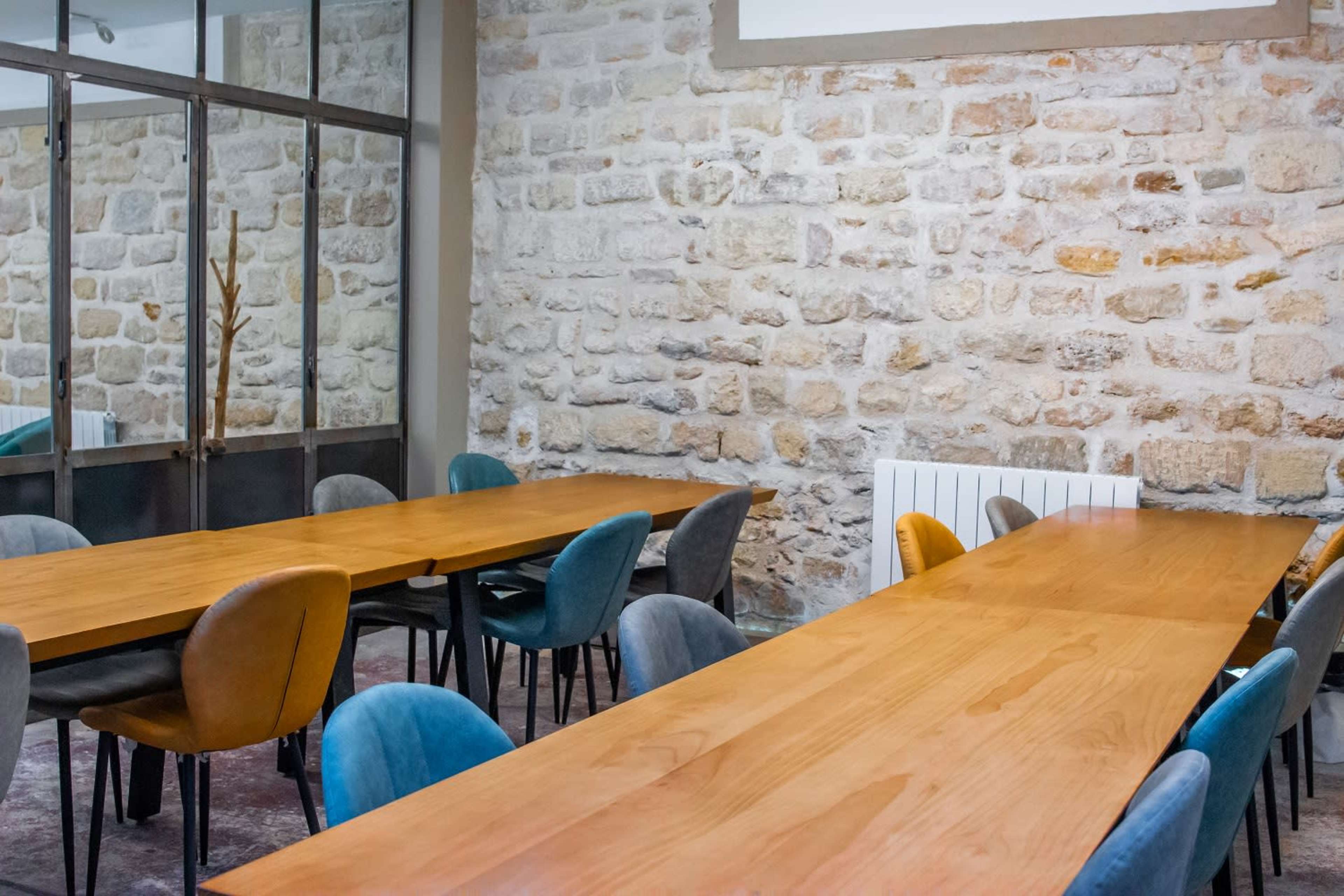 A spacious room with wooden tables and chairs set against a stone wall.