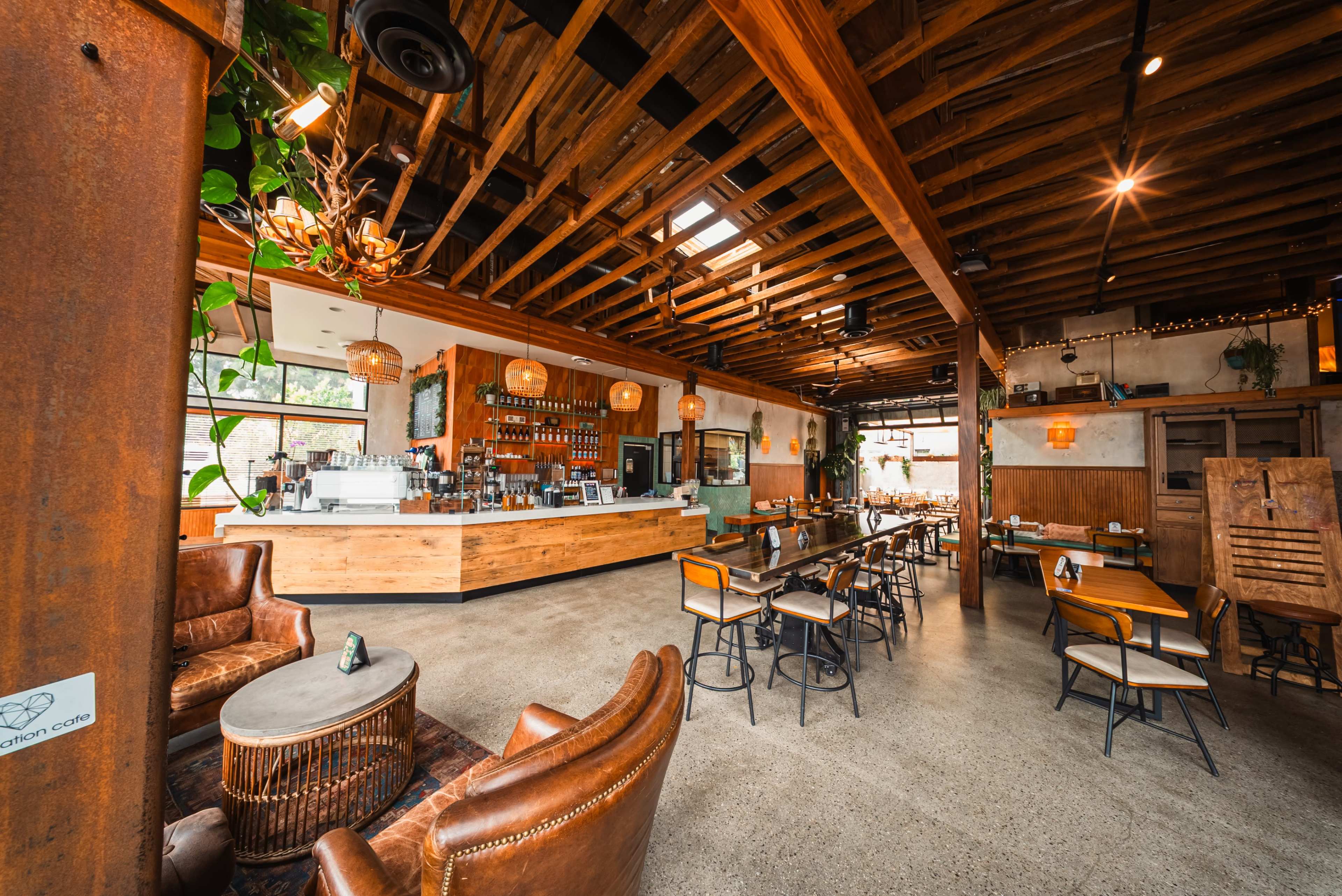 The image shows a spacious, rustic café with wooden ceilings, a bar area, and various seating arrangements, including leather chairs and tables.