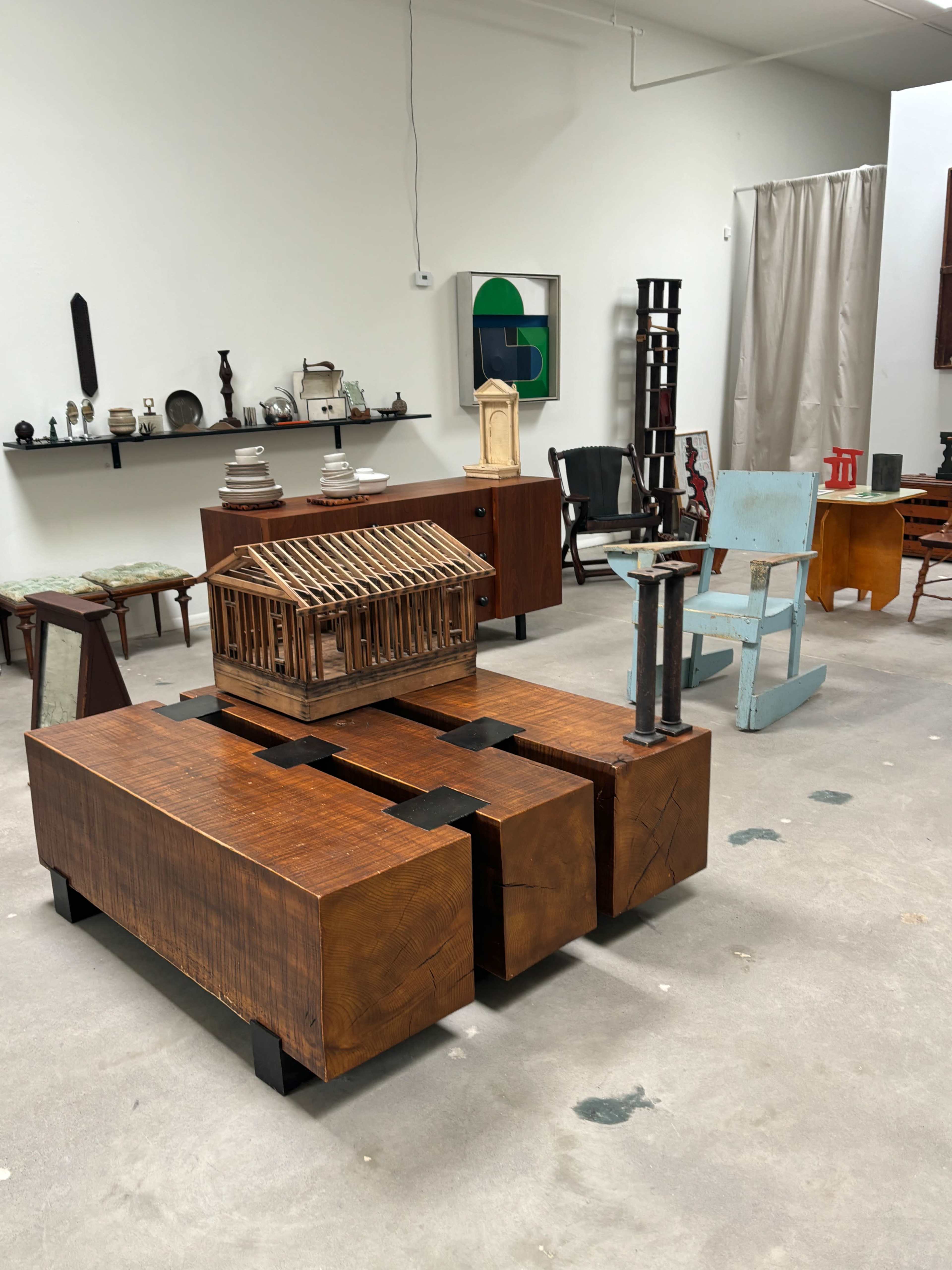The image shows a room filled with various pieces of furniture and decorative objects, including a wooden model house placed on a geometric coffee table.