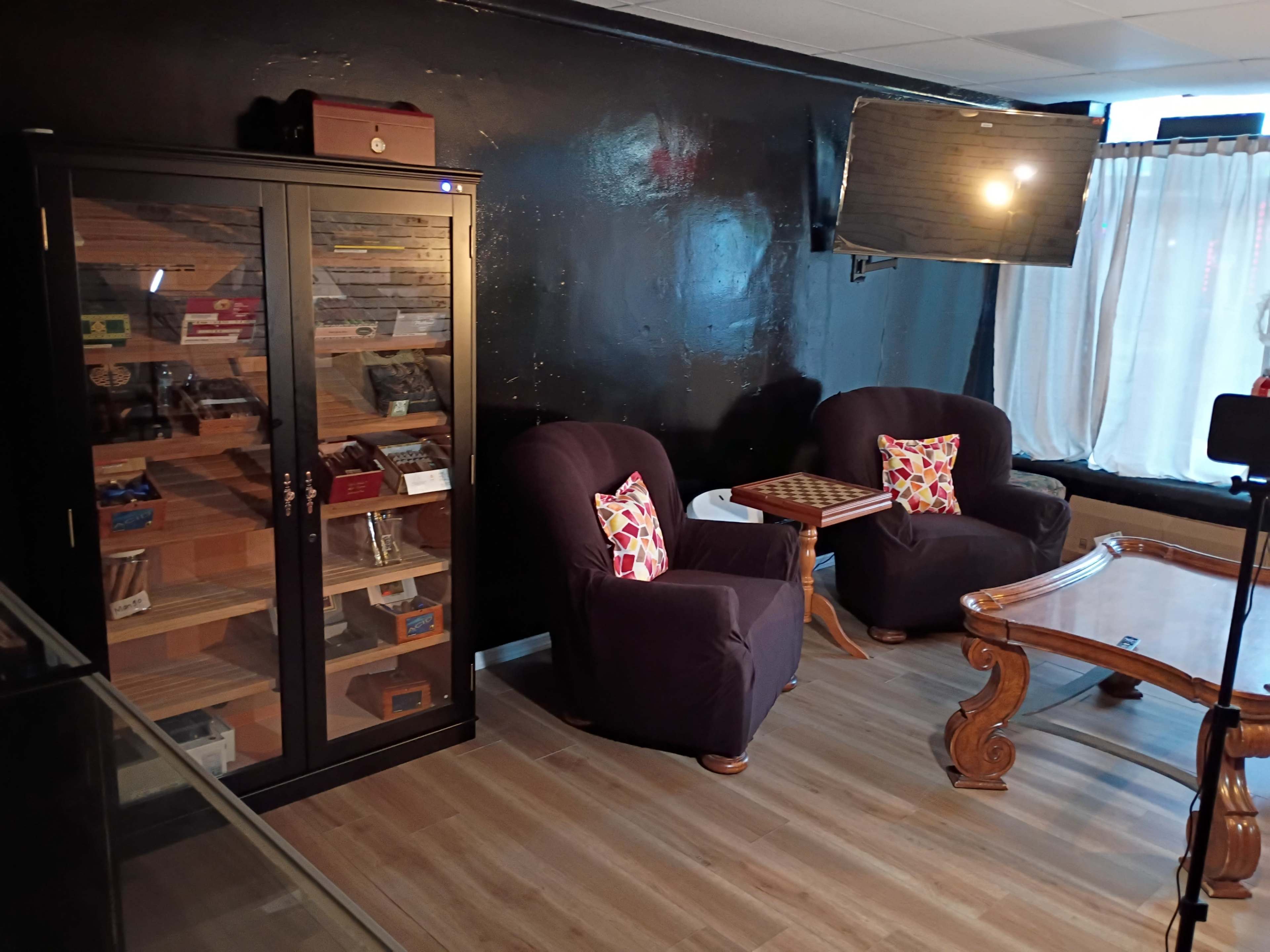 The image shows a cozy seating area with two upholstered chairs, a wooden table, and a display cabinet filled with various items.