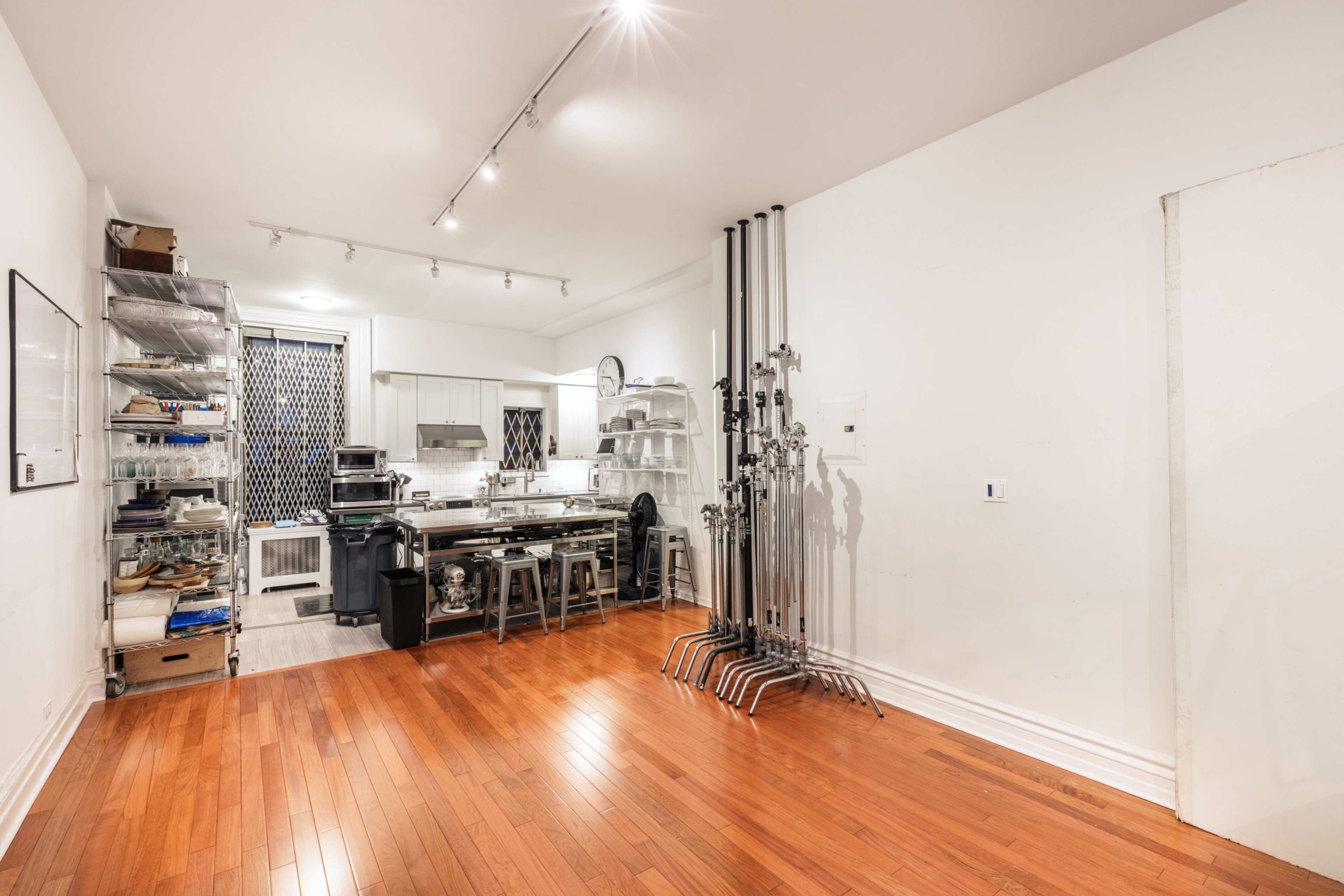 A spacious kitchen area with wooden flooring, stainless steel appliances, and metal shelving units along the wall.
