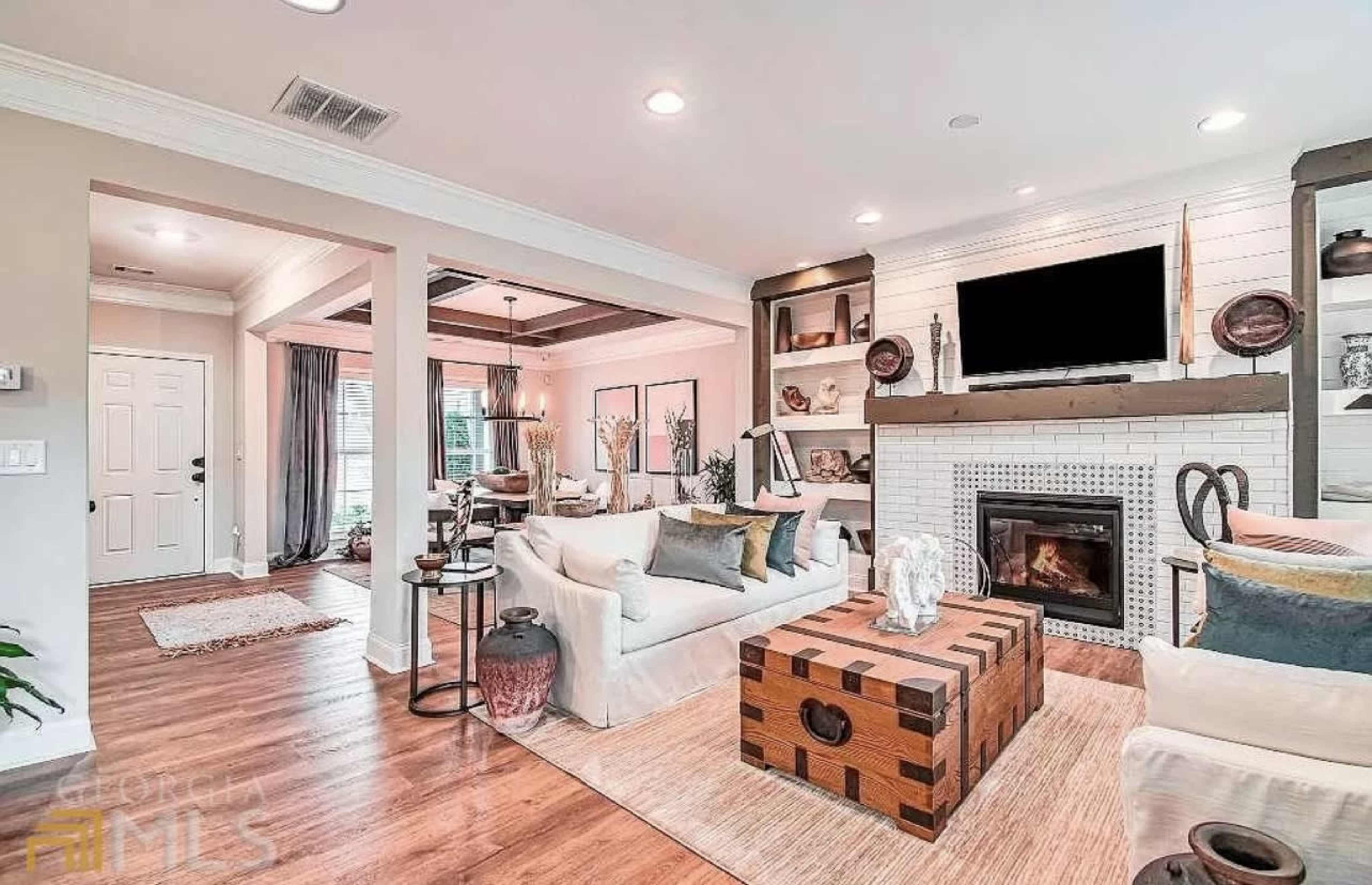 The living room features a white couch, a wooden coffee table, built-in shelves, and a fireplace, with a television mounted above it.