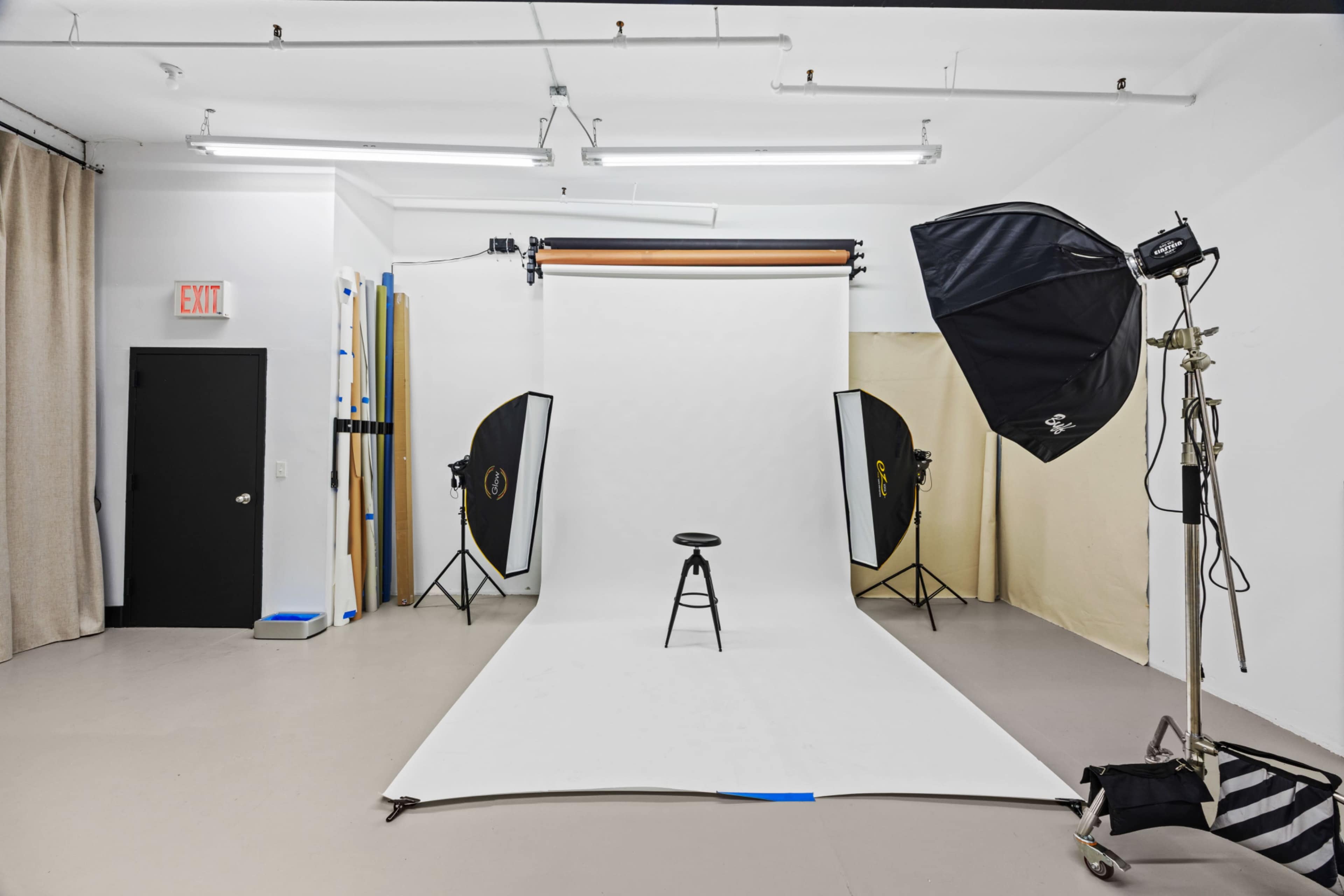 The image shows a photography studio equipped with a white backdrop, a stool in the center, and various lighting equipment on either side.