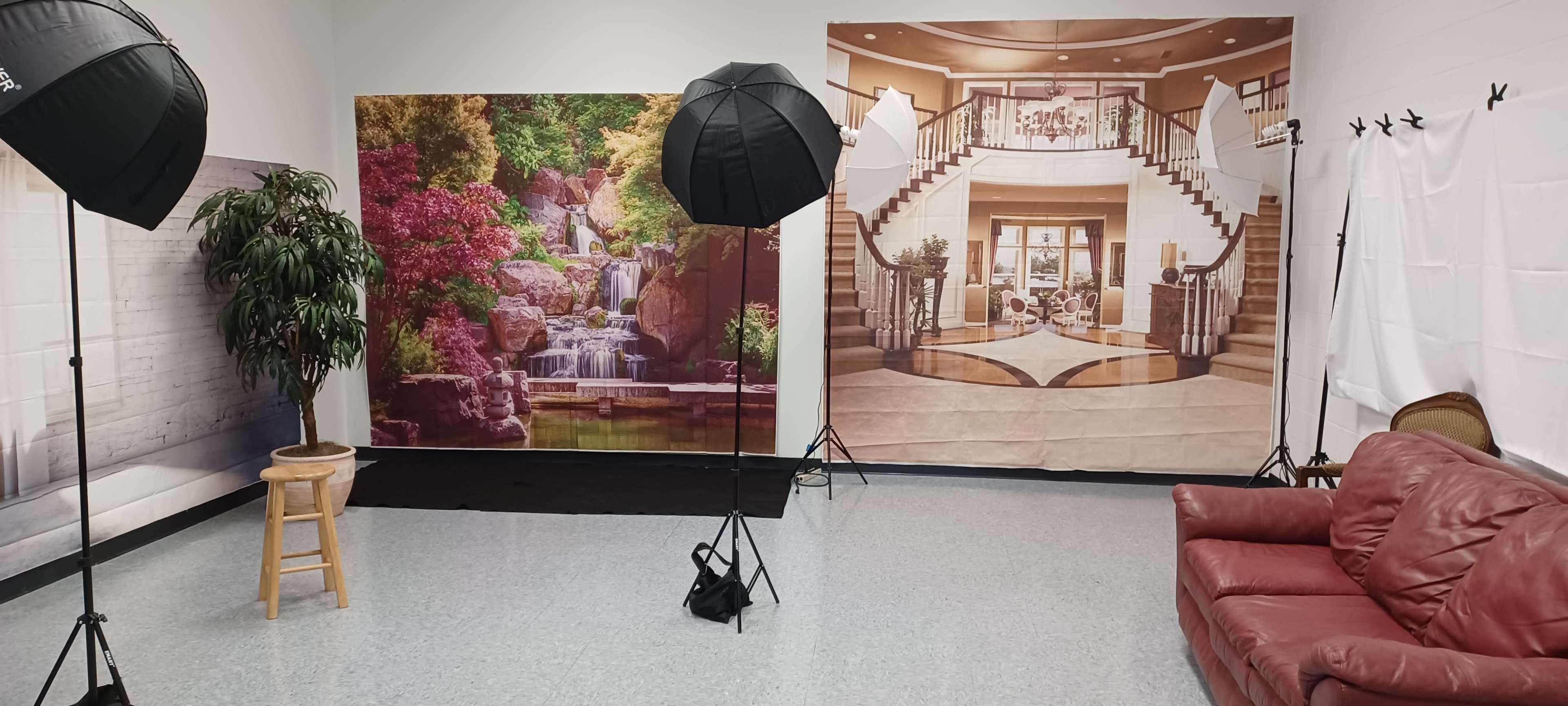 A photo studio setup with large backdrops depicting a decorative indoor space and a scenic garden, accompanied by lighting equipment and a wooden stool.