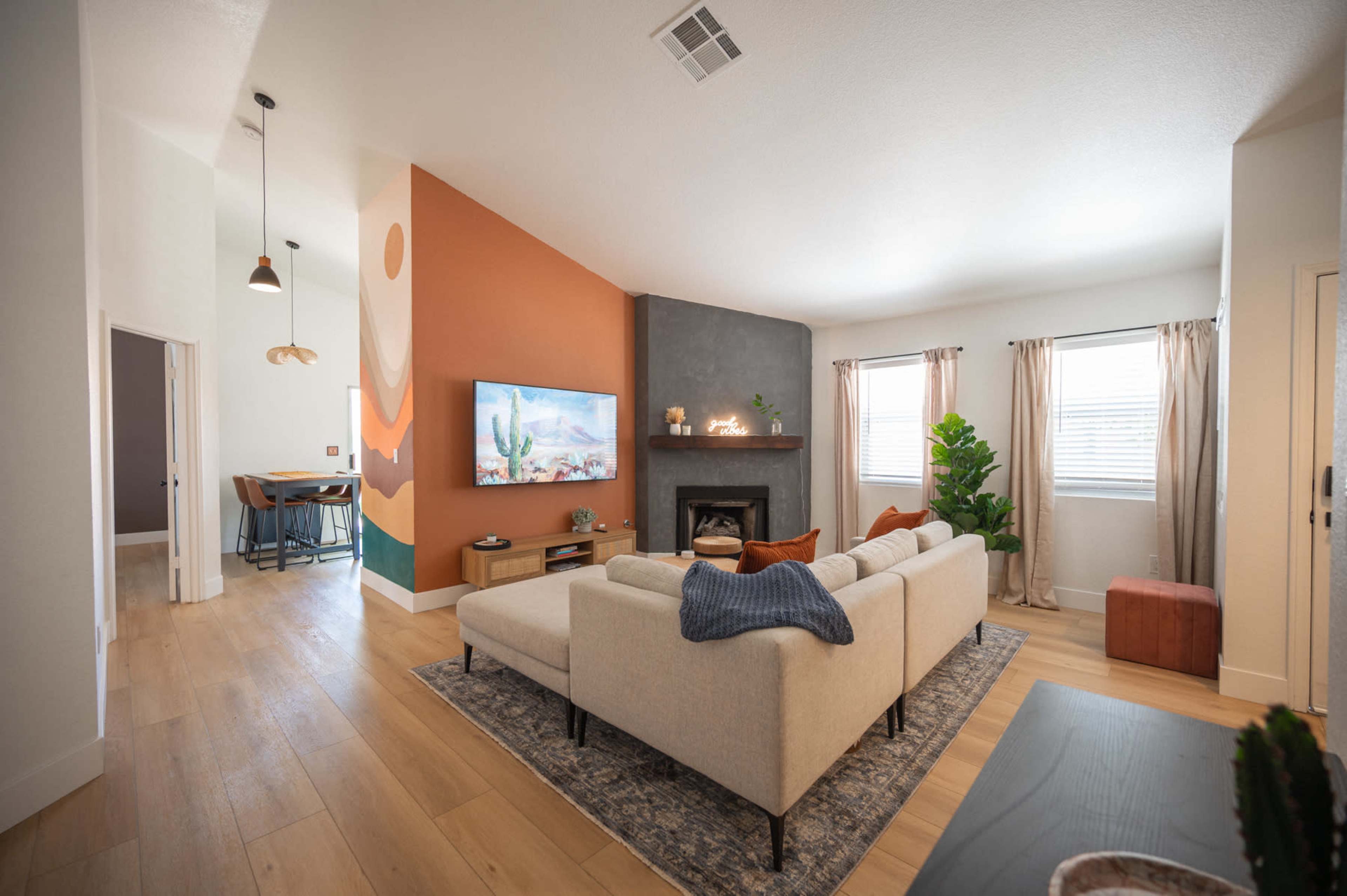 The image shows a modern living room with a sectional sofa facing a fireplace and a large TV, complemented by artwork on the walls and natural light from the windows.
