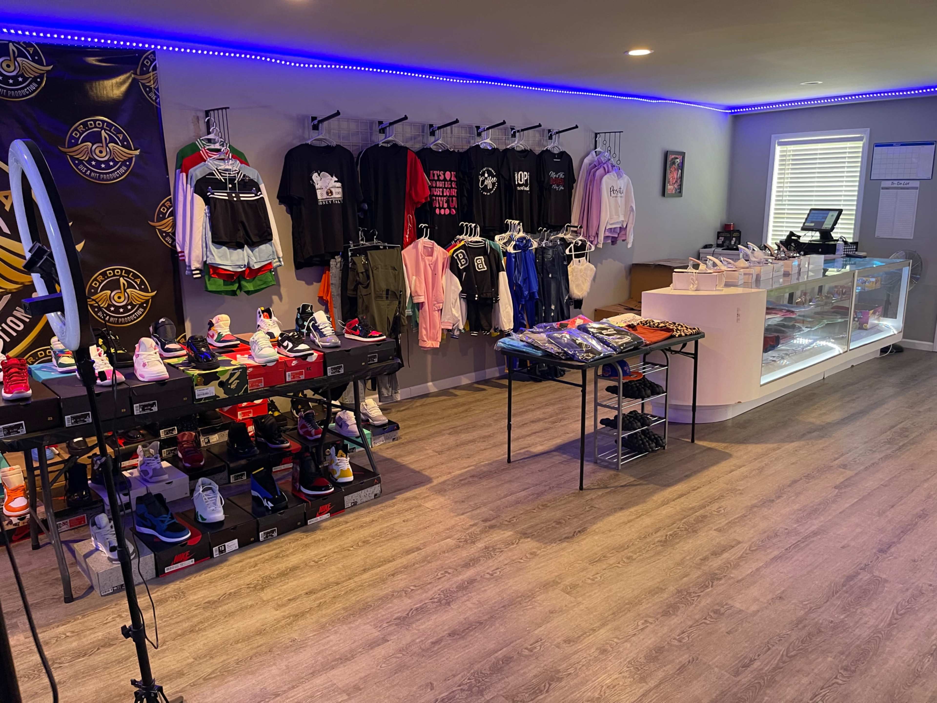 The image depicts a modern retail space showcasing various clothing and sneaker items displayed on racks and tables, with vibrant lighting accentuating the merchandise.
