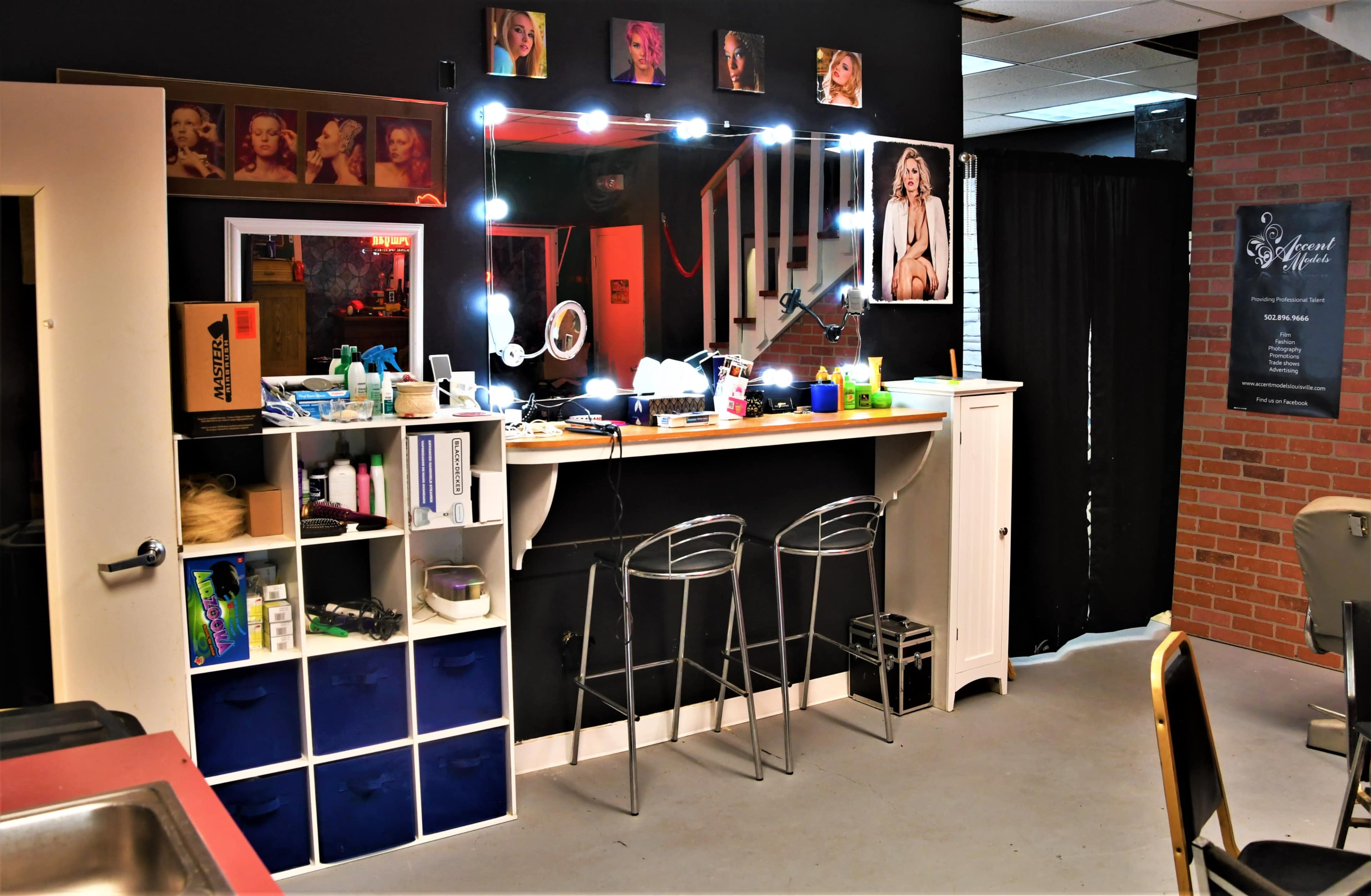 A modern salon setup featuring a mirror with bright lights, a counter with stools, and various beauty products organized on shelves.