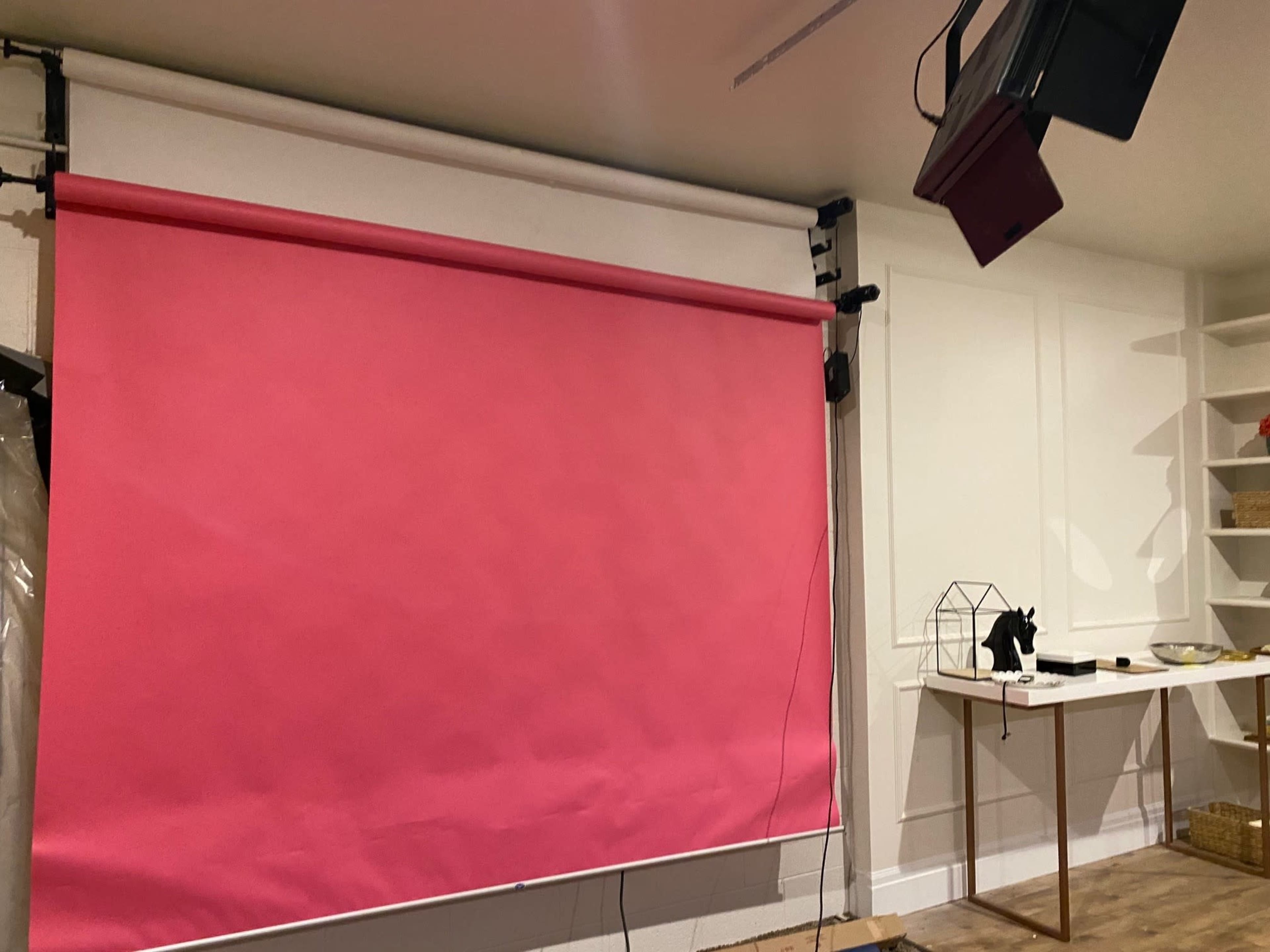 A room with a pink backdrop mounted on a wall and a white table with decorative items beside it.