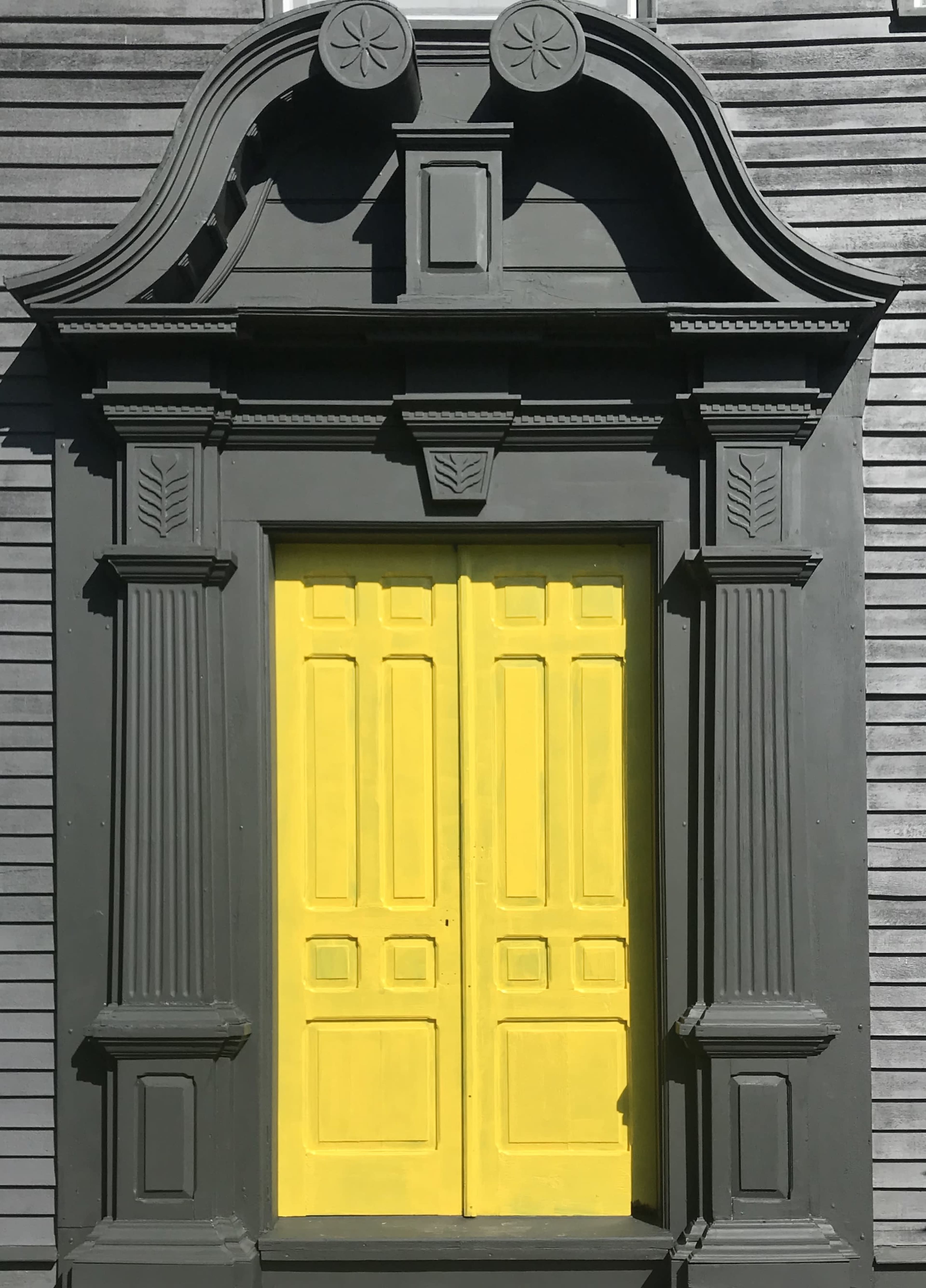 A prominent architectural doorway with a dark exterior and bright yellow double doors, framed by intricate columns and decorative moldings.