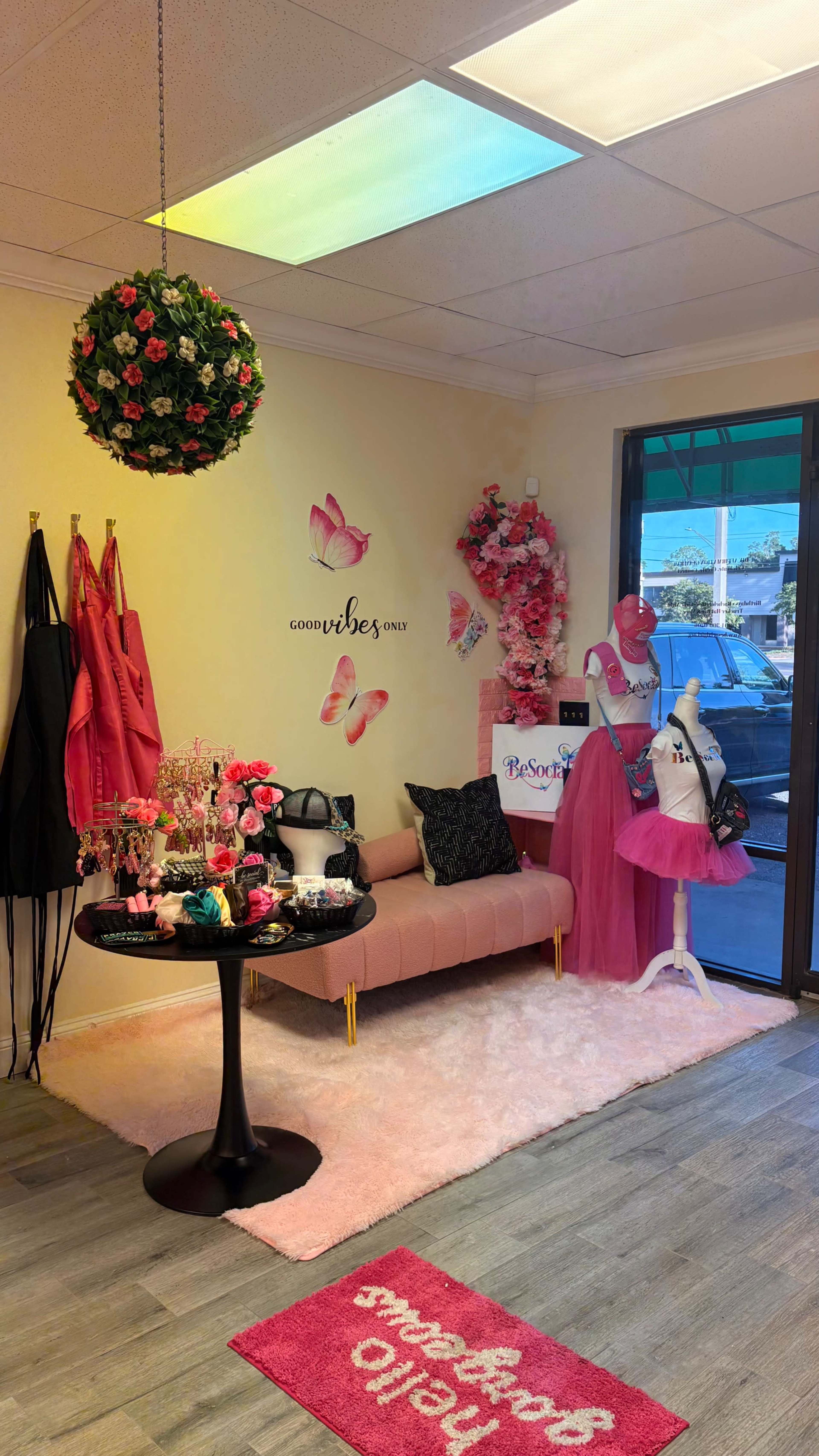 The image shows a colorful boutique interior with a pink couch, a black table, and various pink and floral decorations on the walls.
