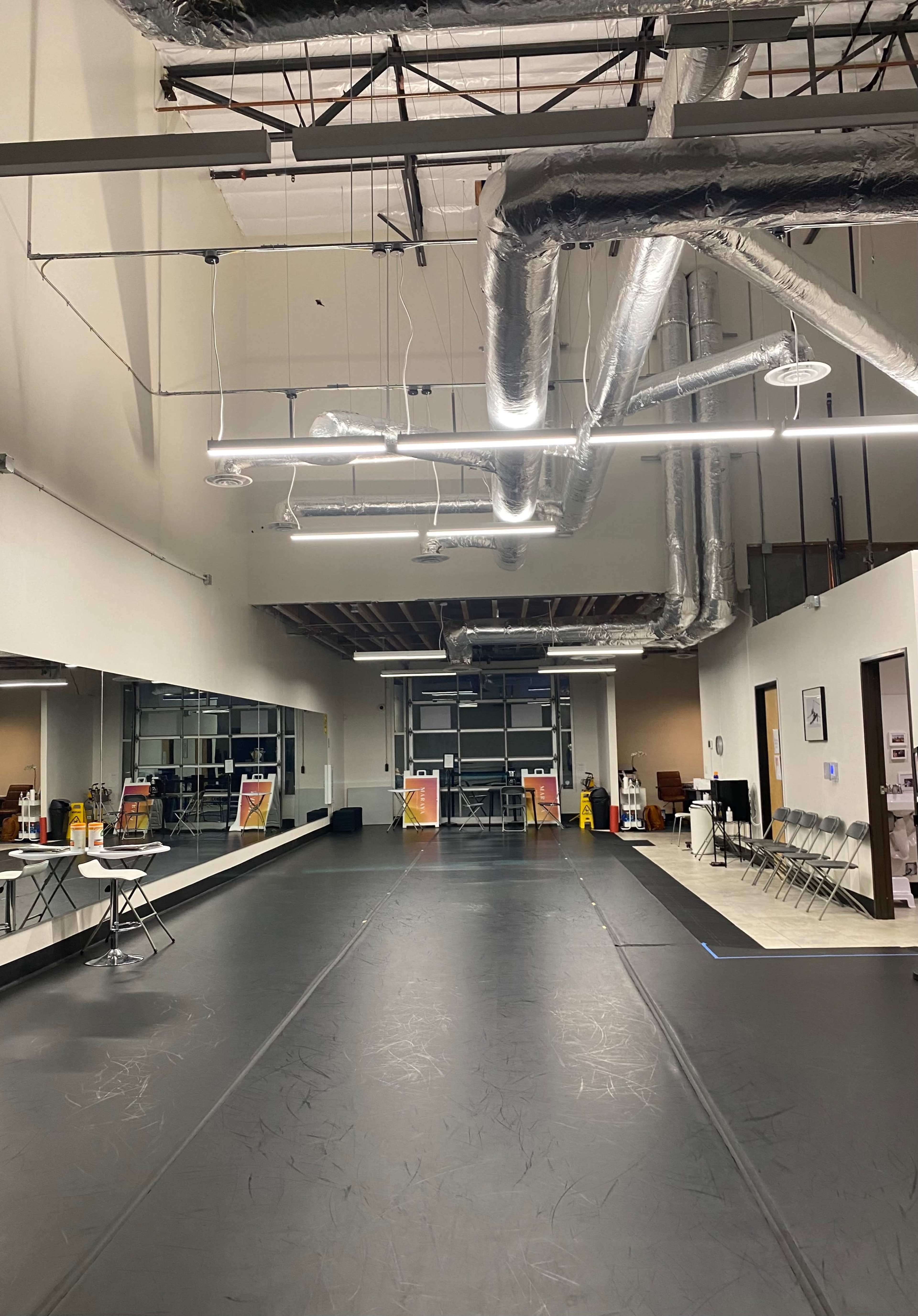 An empty floor space of a dance studio, featuring mirrors along one wall and bright overhead lighting.