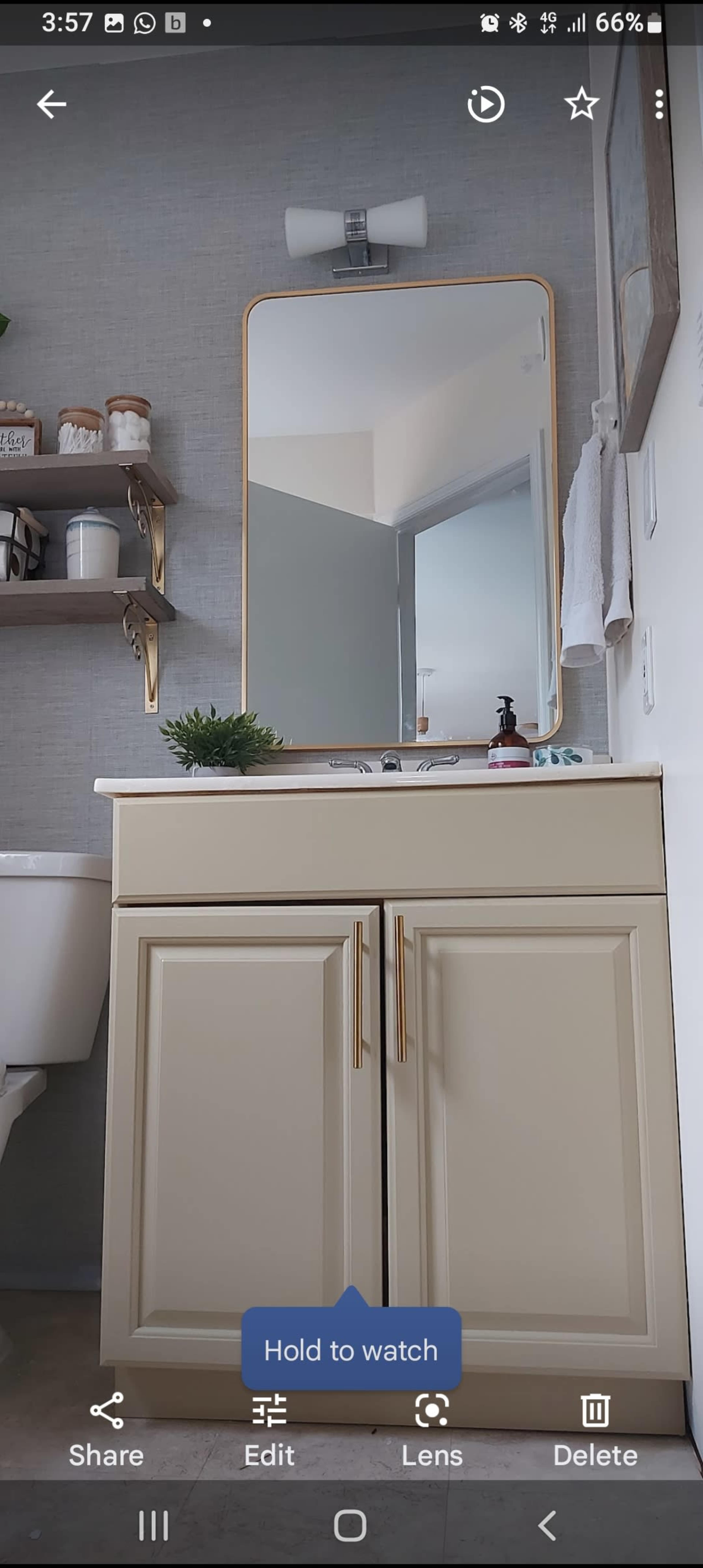 A bathroom scene features a vanity with a large mirror above it and shelves displaying various items.