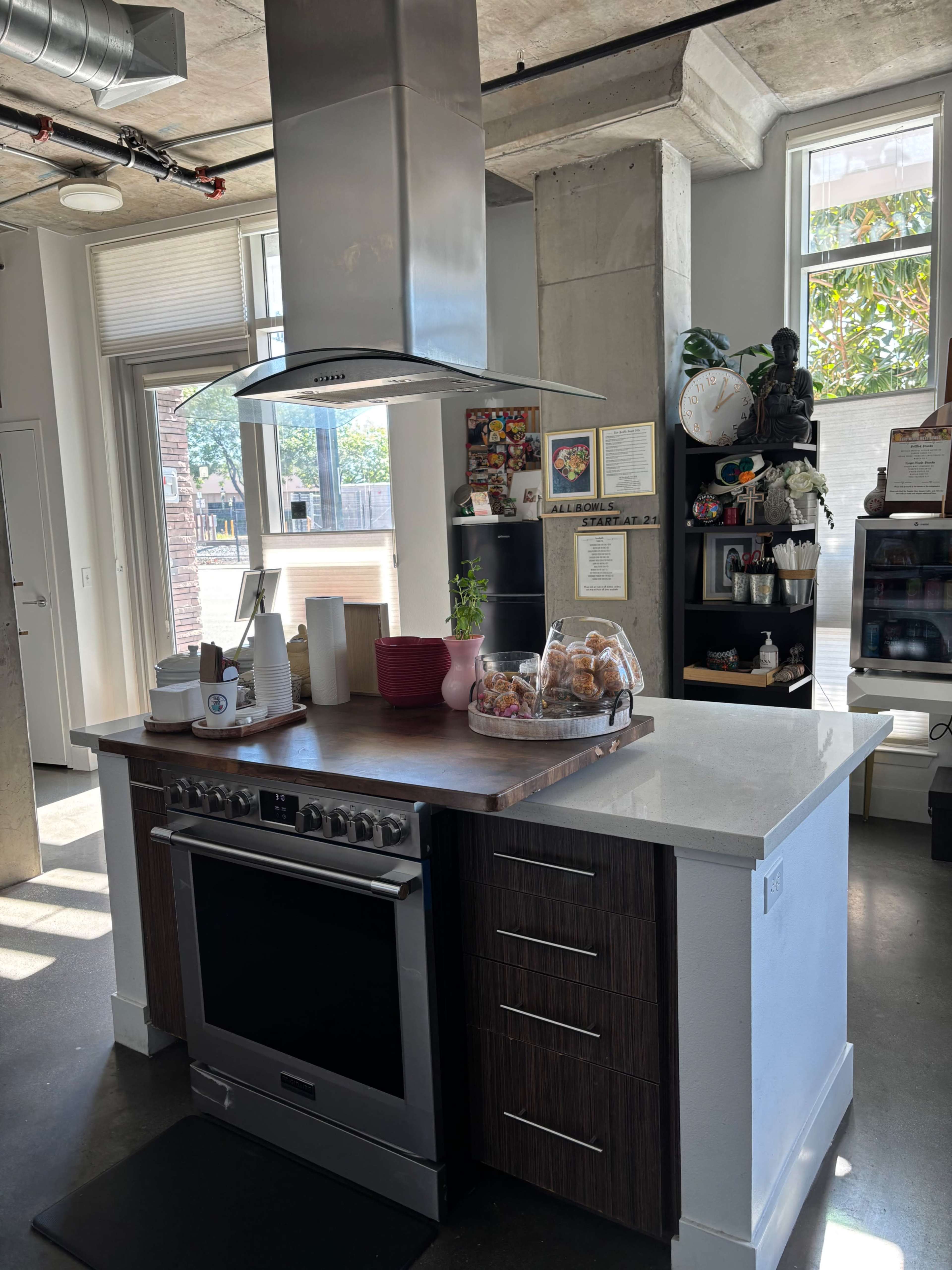 The image features a modern kitchen with an island that includes a stainless steel oven, a range hood above, and a decorative bowl of fruit on a counter.