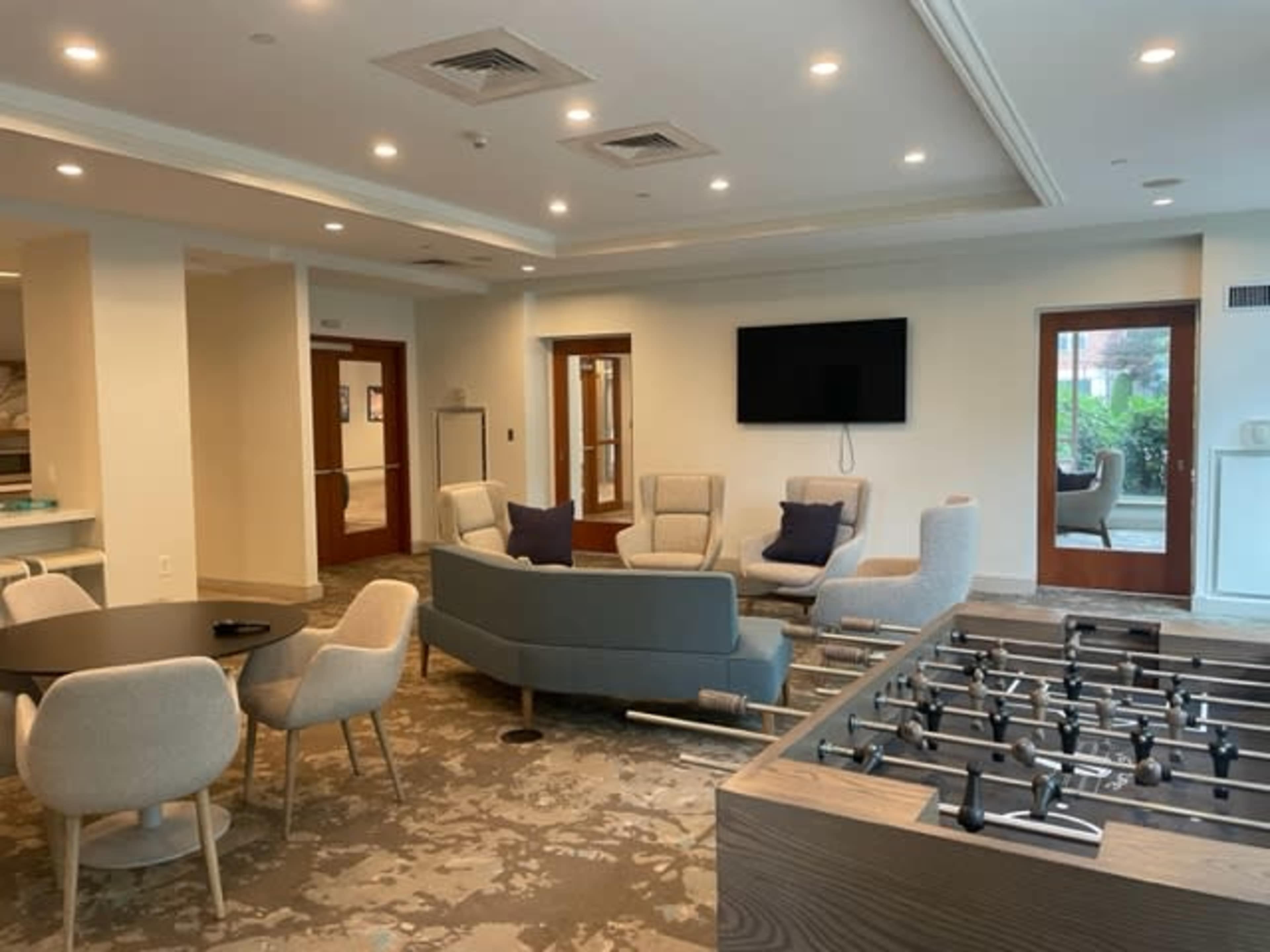 A modern lounge area with seating, a television on the wall, and a foosball table in one corner.