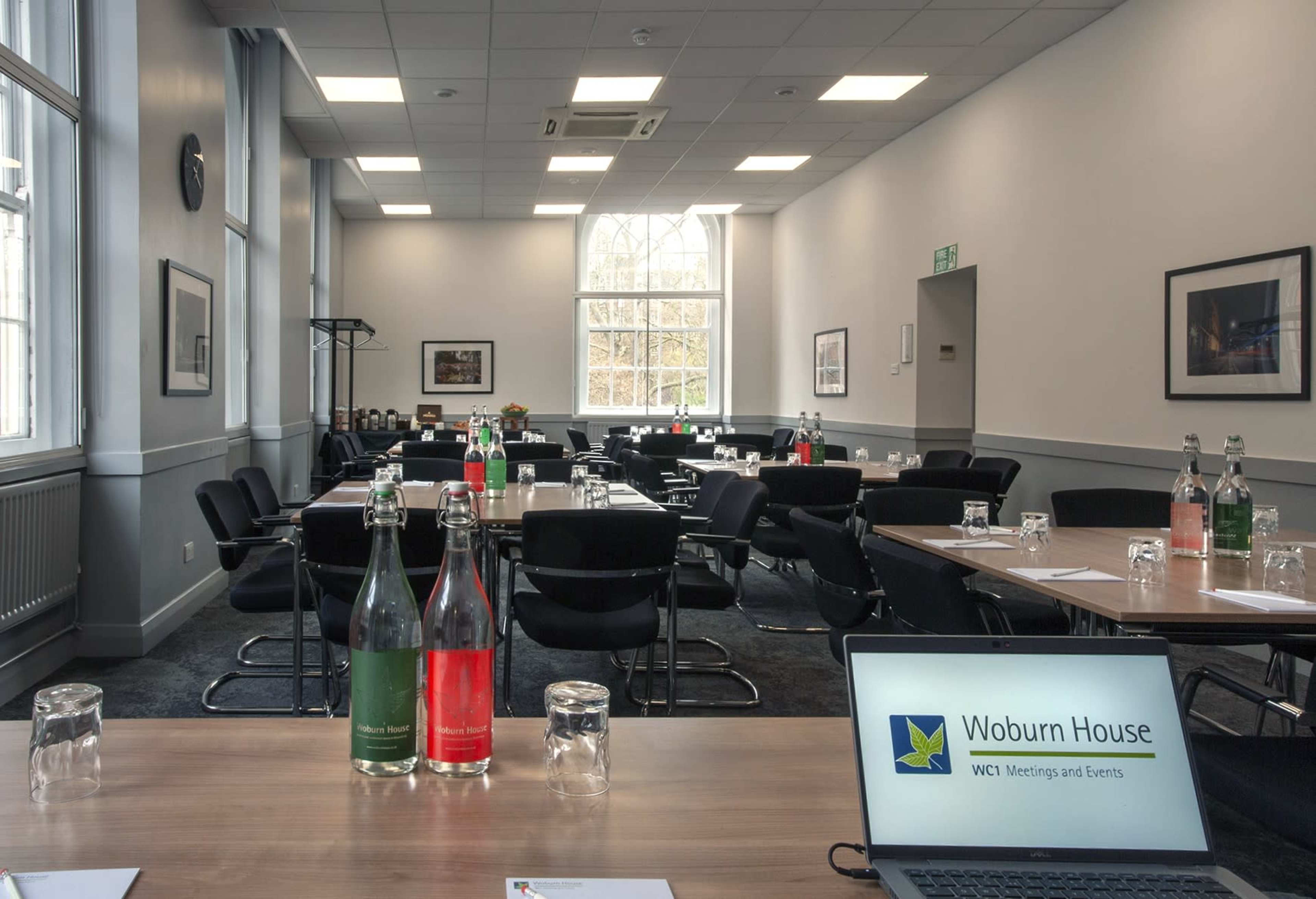 A conference room is set up with multiple tables and chairs, featuring refreshments on the side and a laptop displaying event information.