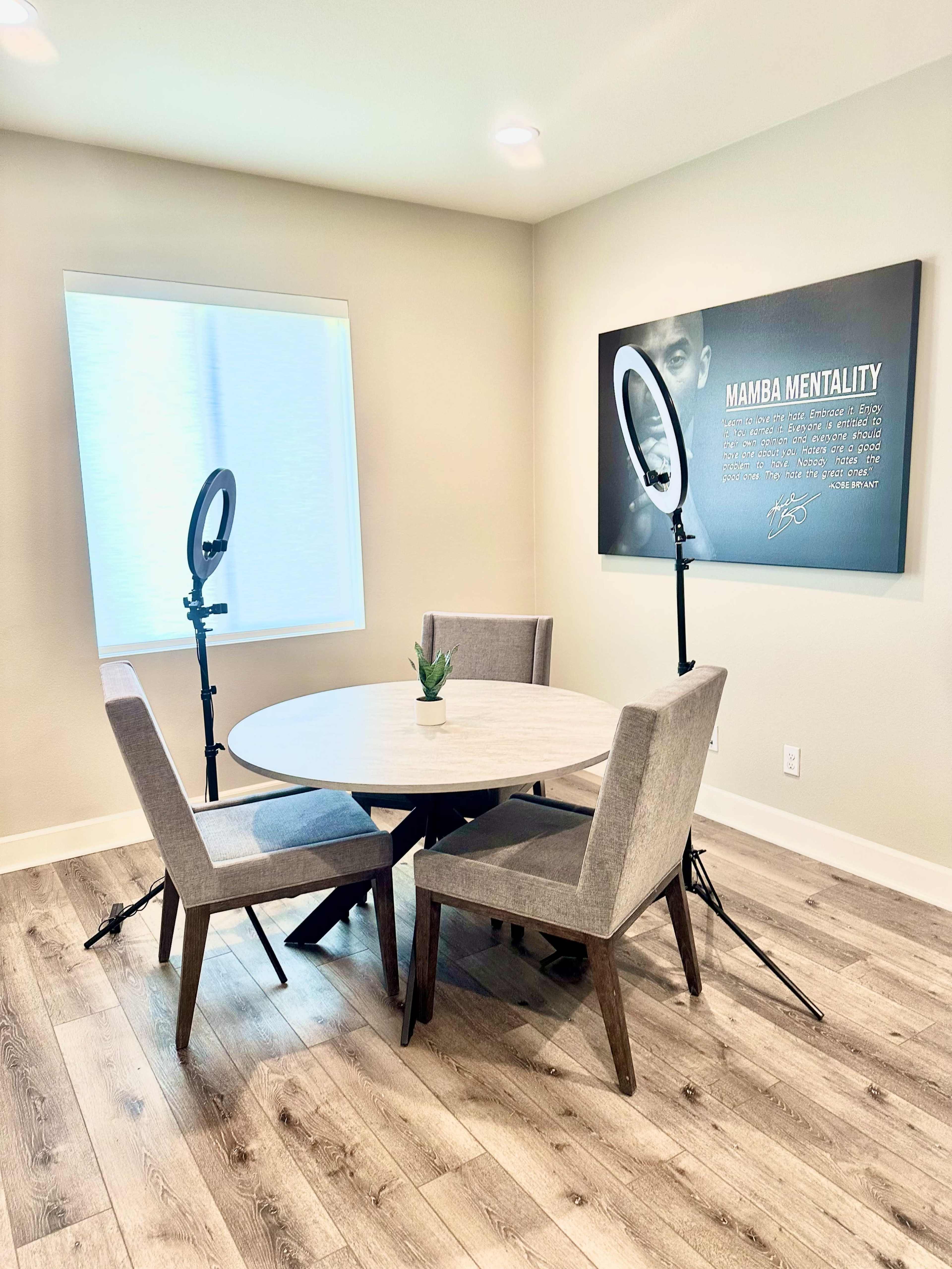 A round table surrounded by four chairs is positioned in a well-lit room featuring a motivational poster on the wall.