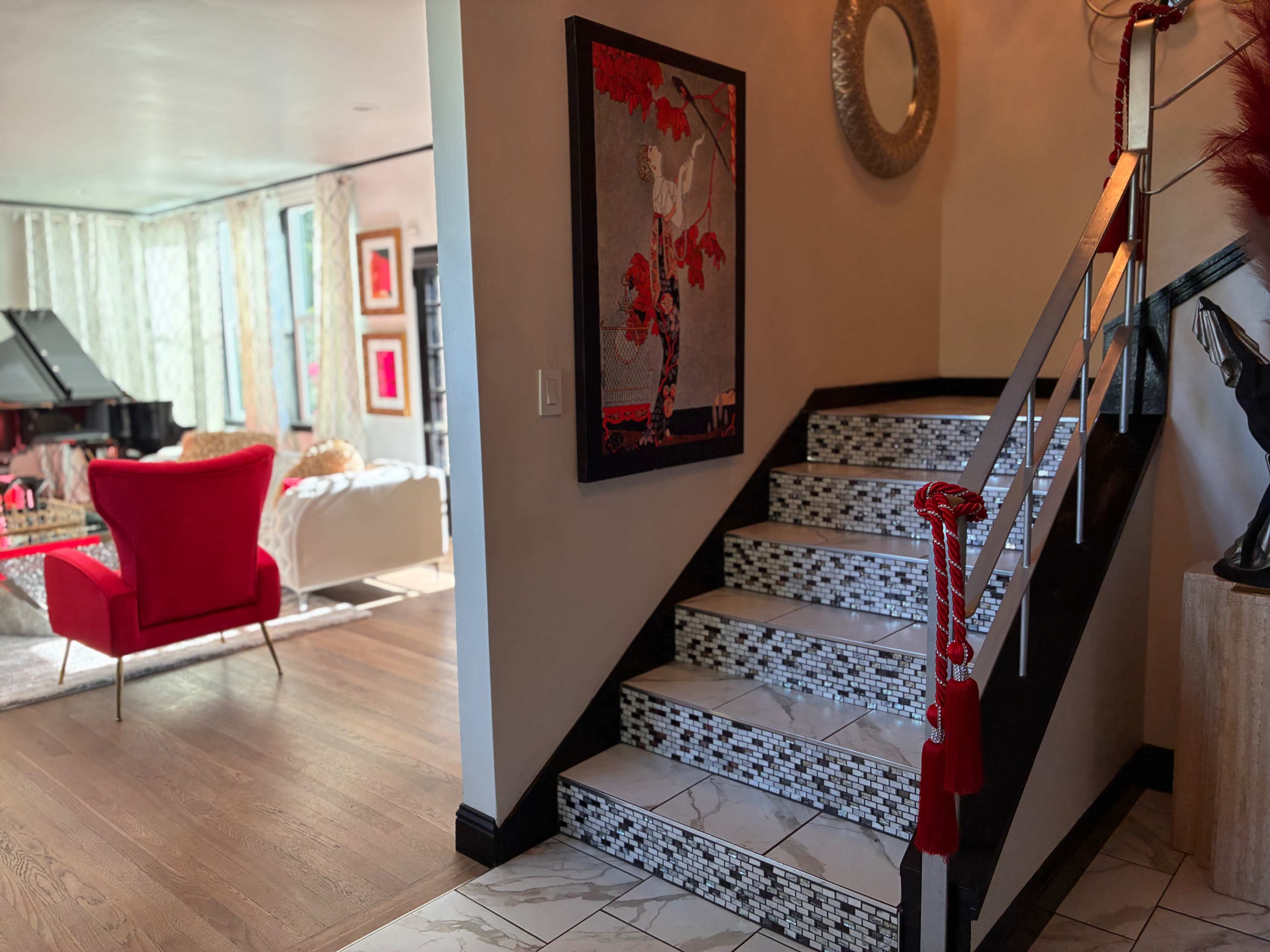 A staircase with decorative tiles leads up to a living area that features a grand piano and red accent furniture.