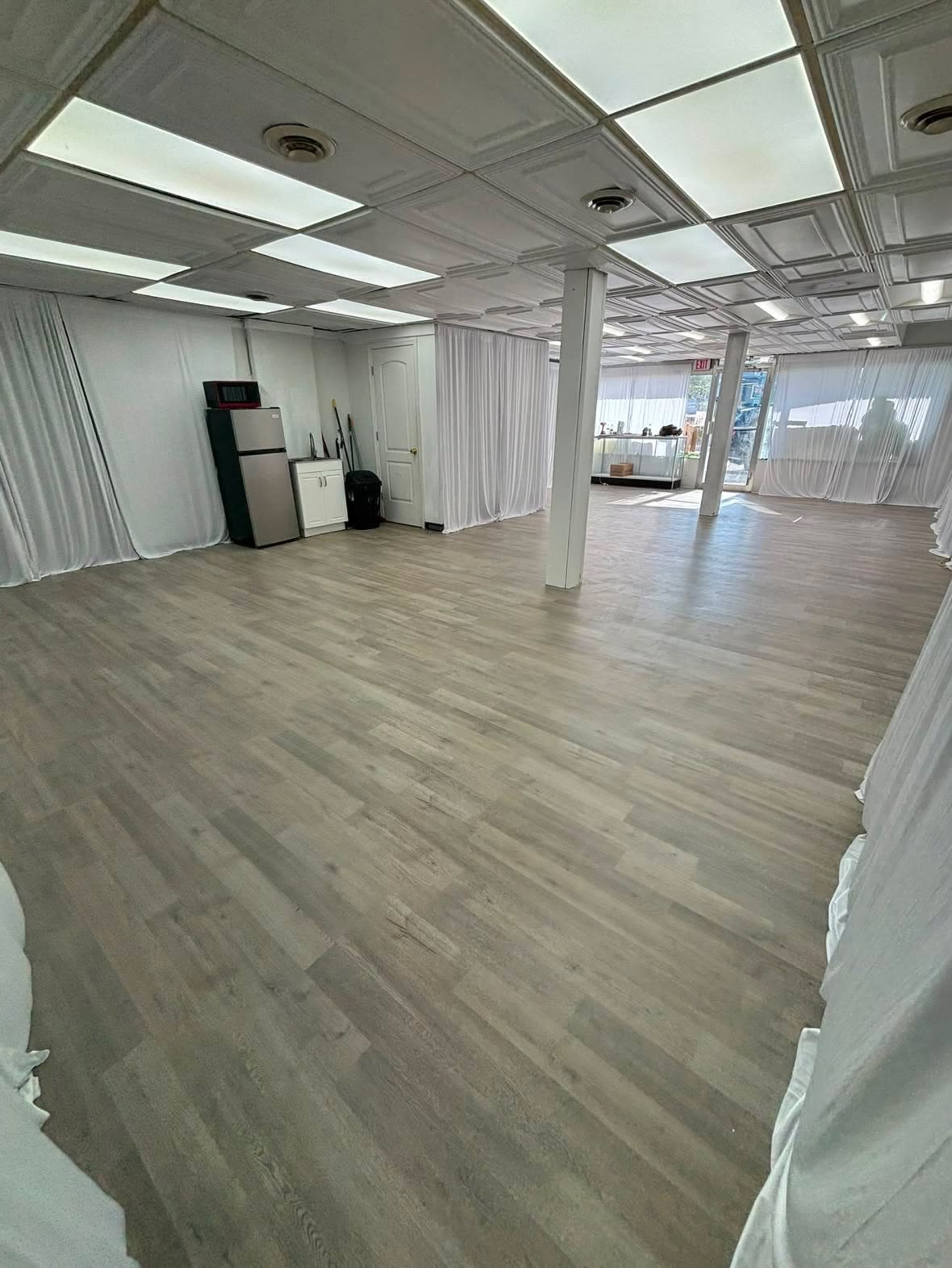 The image shows an empty room with light-colored flooring, white drapes covering the walls, and fluorescent ceiling lights.