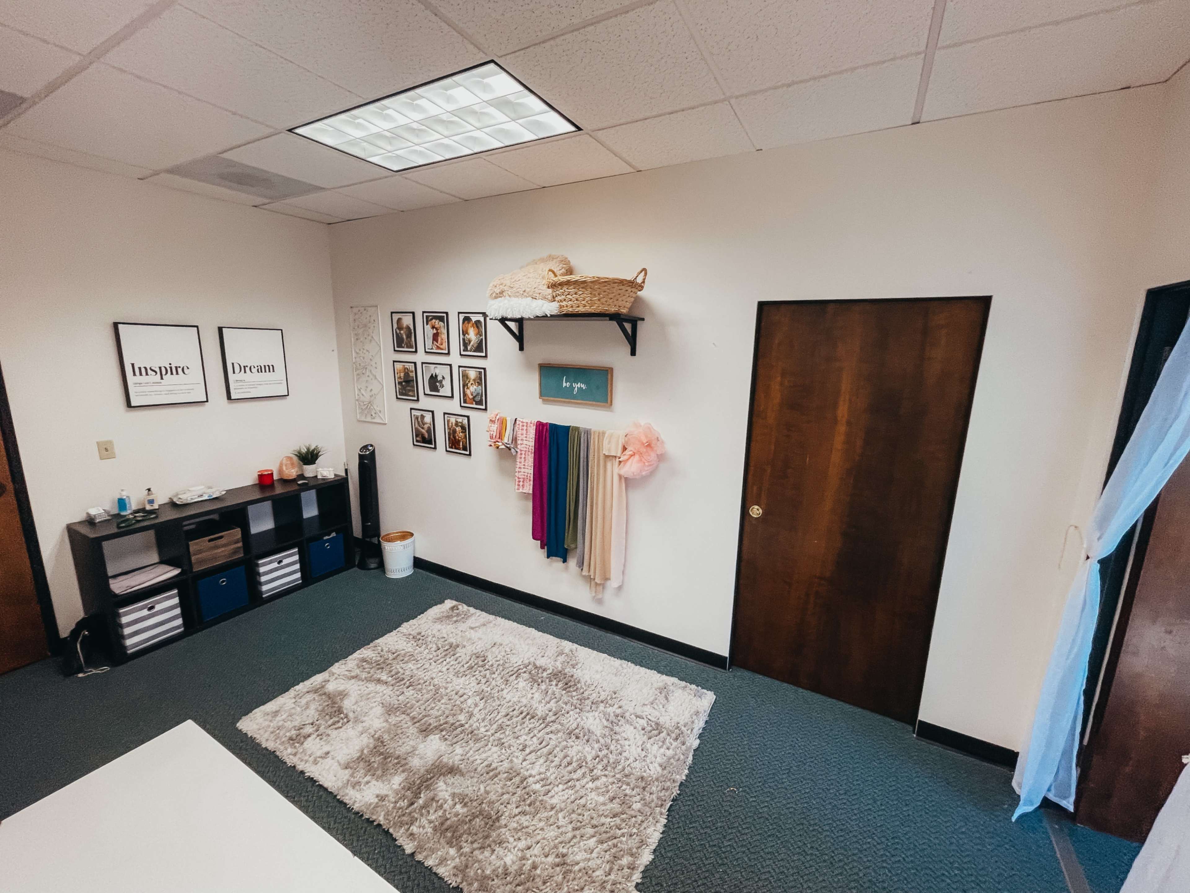 The image shows a well-organized room featuring a shelf with baskets, a wall adorned with framed photos, and a rug on the carpeted floor.