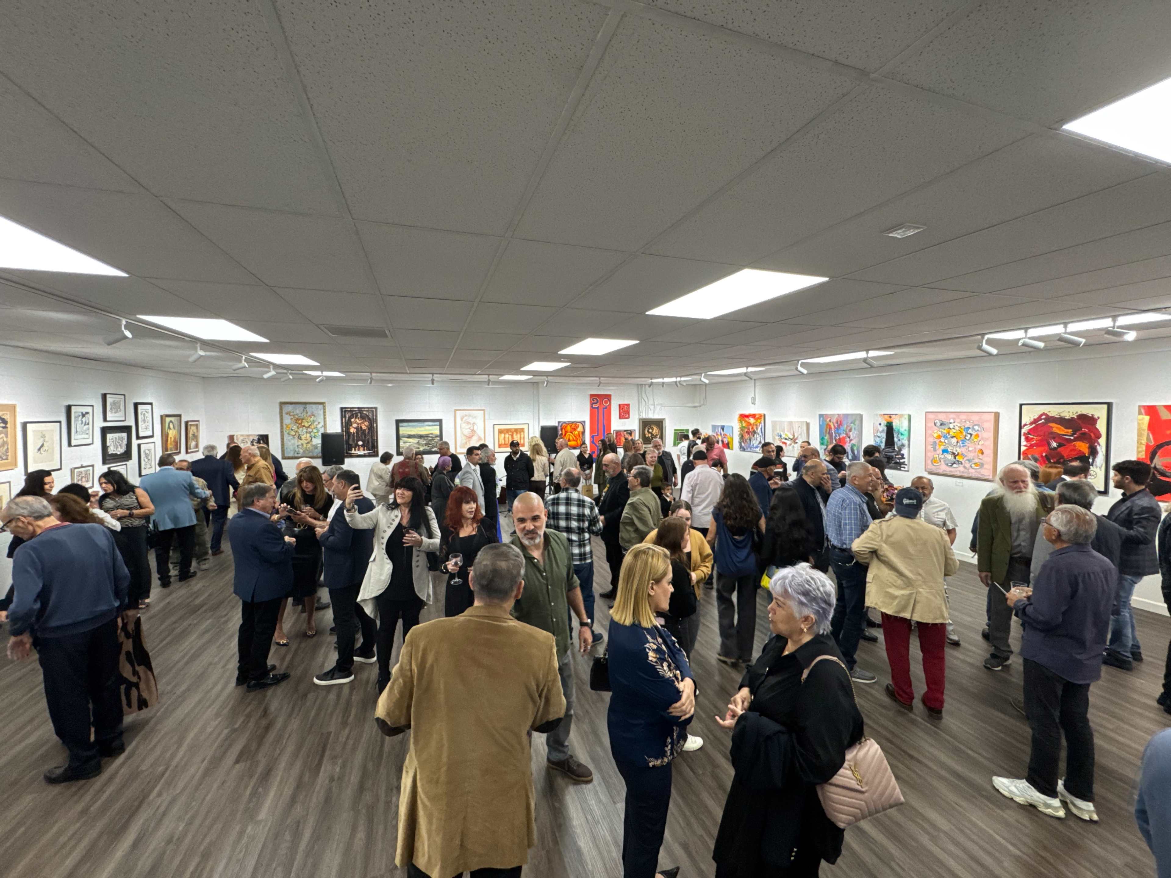 A large group of people is gathered in an art gallery, viewing various artworks displayed on the walls.