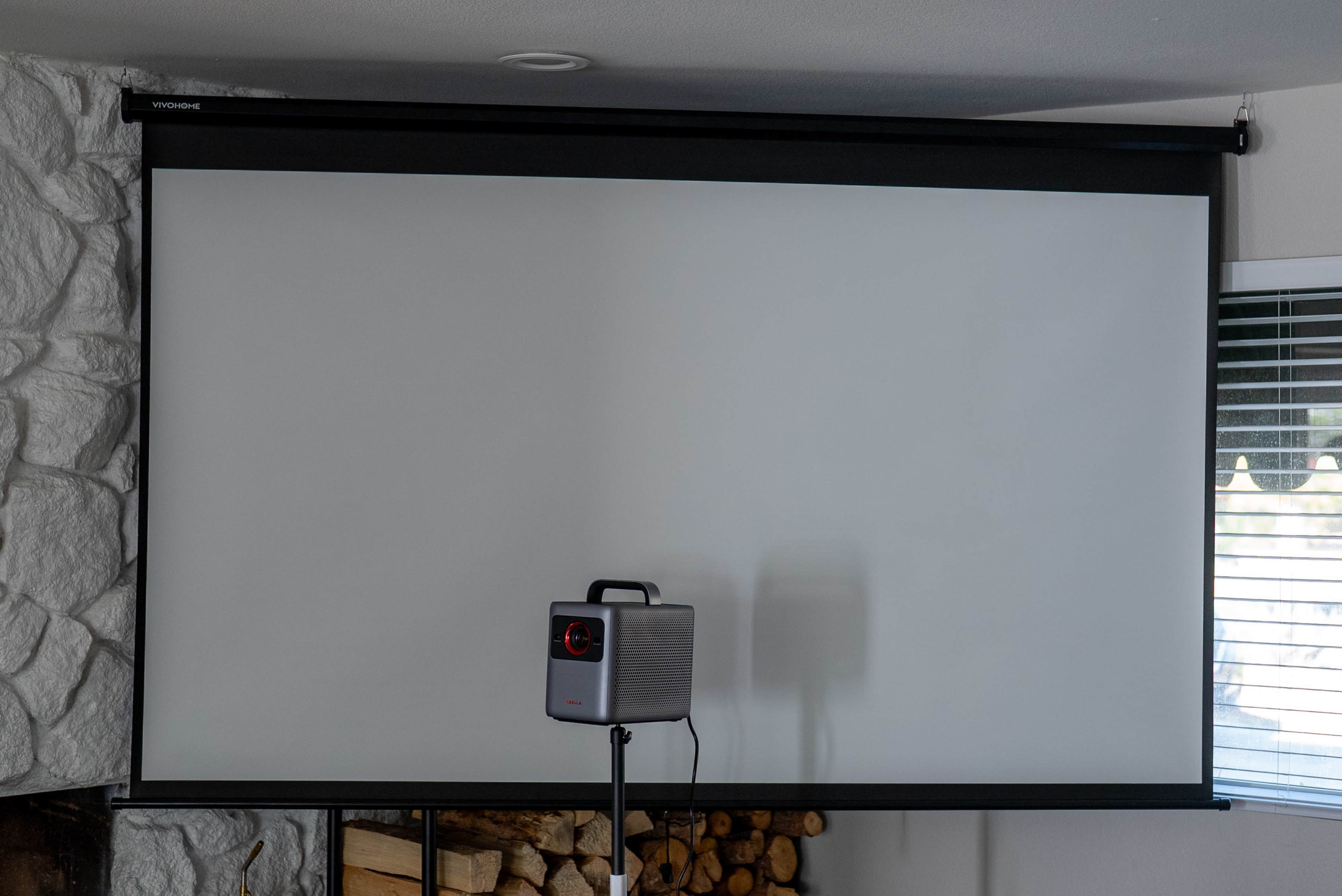 A retractable projector screen is mounted on a wall above a portable projector on a stand.