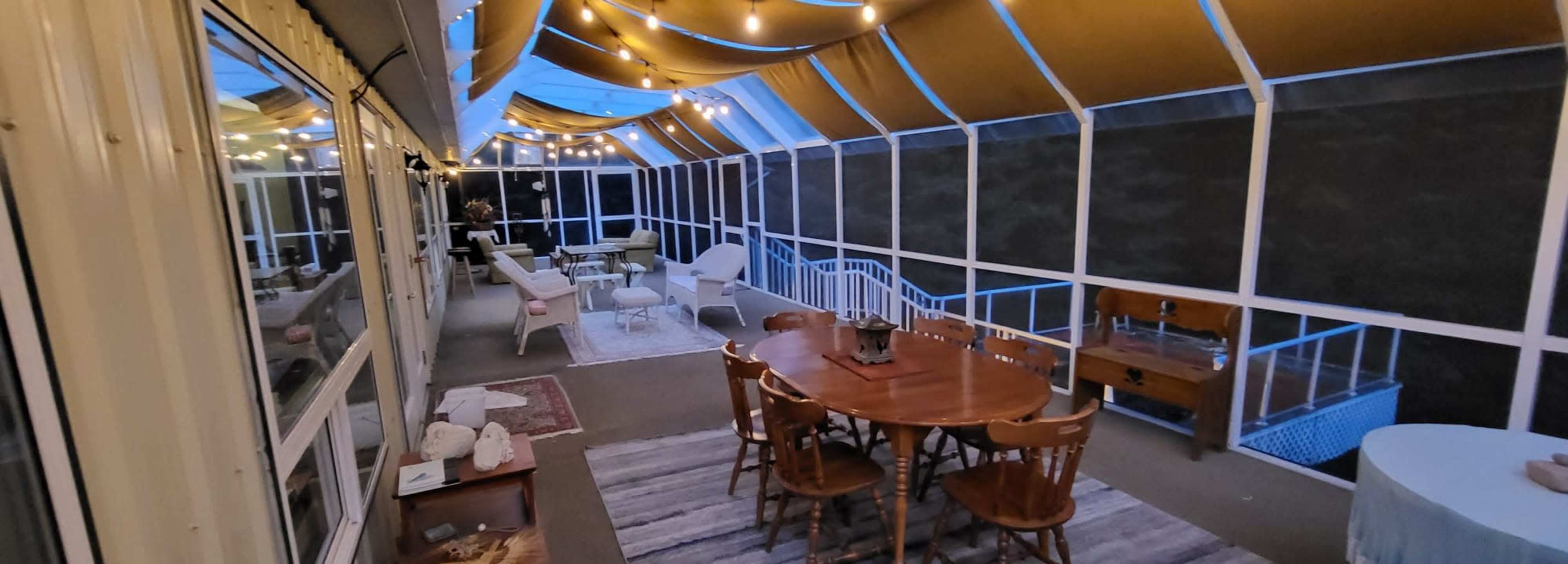 A spacious screened porch with a dining table, seating areas, and string lights overhead.